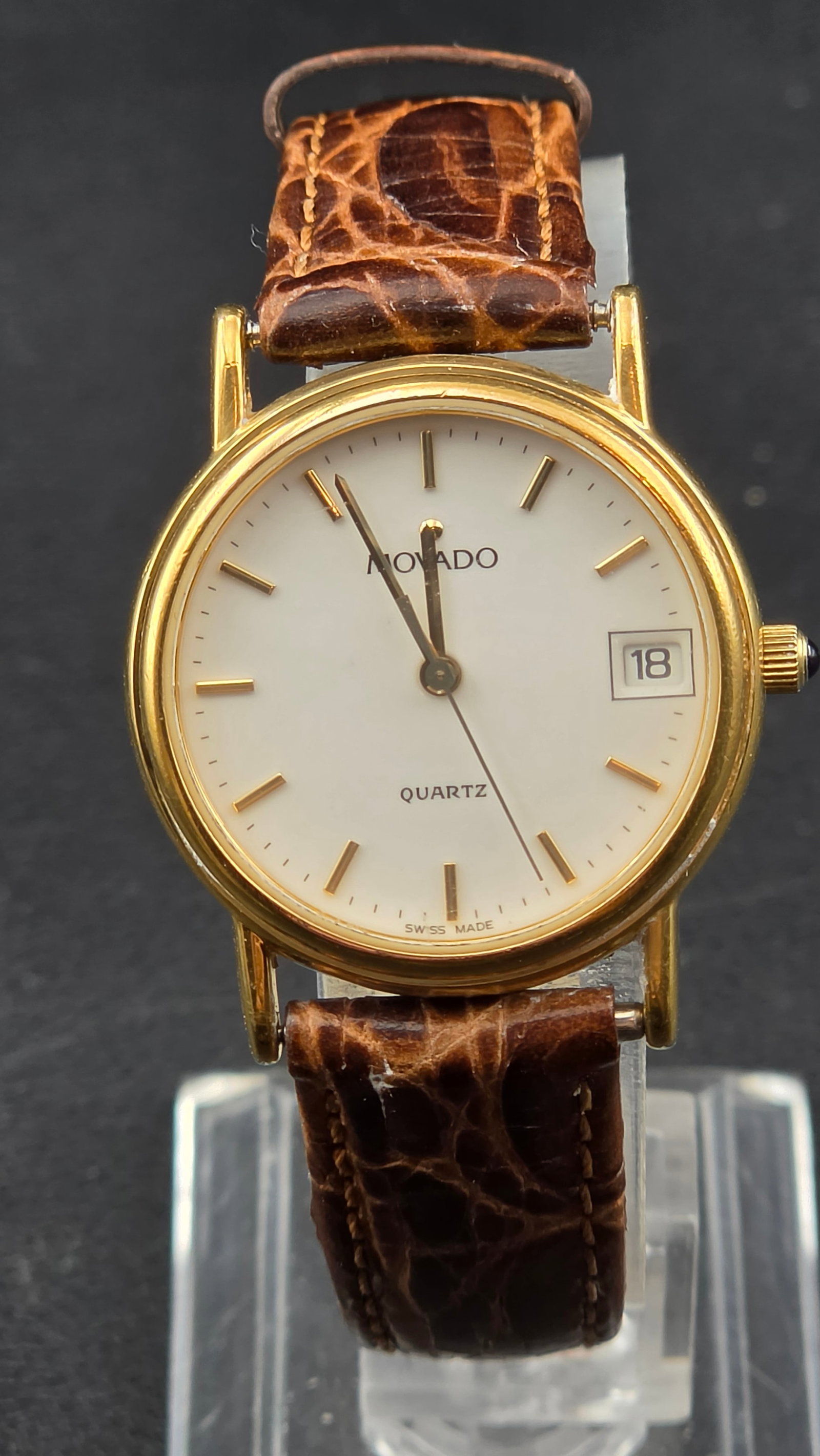 Movado ESQ 87-A6-825K Quartz Gold Tone Date Watch 28mm Swiss Made Running: Movado ESQ quartz wristwatch featuring a clean white dial with applied gold-tone markers and date window at 3 o’clock. Slim gold-tone case with Swiss-made quartz movement and cabochon-style crown de