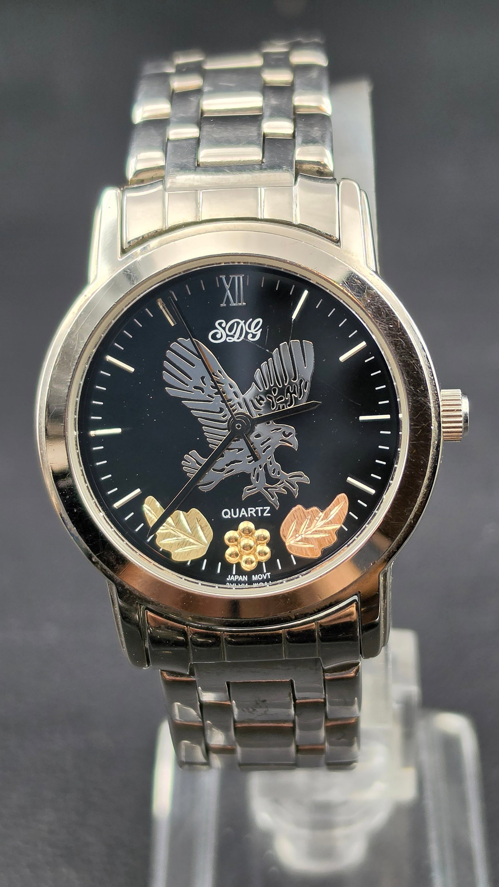 Modern SDG Eagle Dial Quartz Watch 34mm Stainless Steel Bracelet Japan Movt Running: Contemporary SDG quartz wristwatch featuring a bold black dial with raised eagle motif and decorative gold-tone leaf accents. Roman numeral at 12 with applied stick indices and central seconds. Dial m