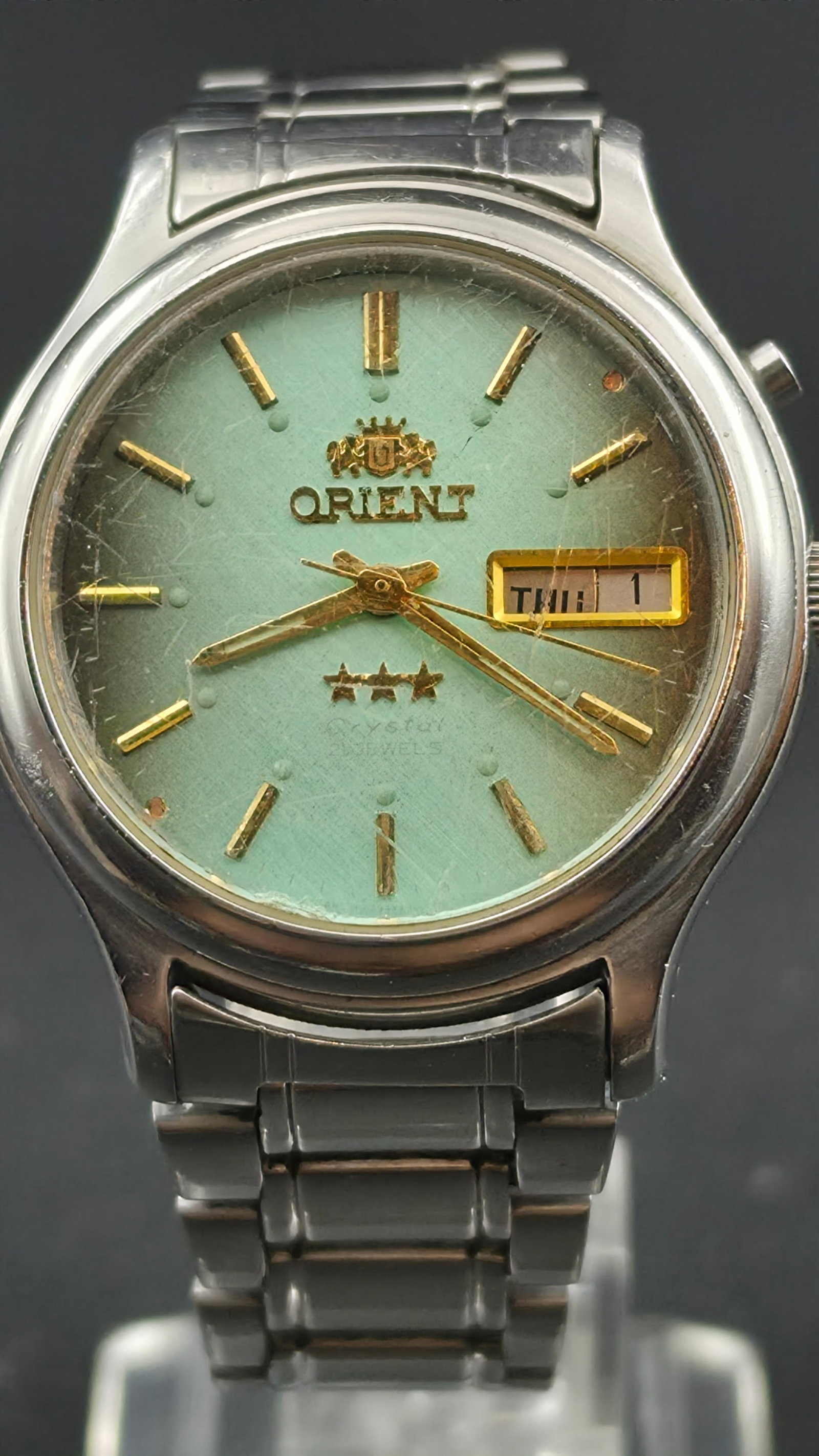 Vintage Orient Three Star Crystal 21 Jewel Automatic Men's Watch Teal Dial Day Date 36mm Runs: for auction is a vintage Orient Three Star Crystal automatic men's wristwatch, made in Japan. This eye-catching timepiece features a distinctive teal green textured dial with gold-tone baton hour mark