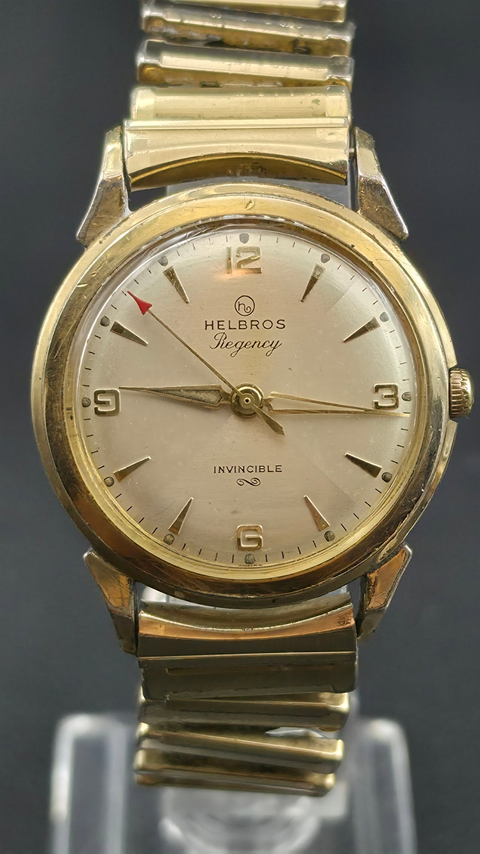 Helbros Regency Invincible Manual Wind Gold Tone 33mm Stainless Back 1960s Runs: This is a vintage Helbros Regency Invincible manual wind watch with a gold tone case measuring 33mm as shown by calipers in the photos. The dial is champagne silver with applied gold sword and baton h