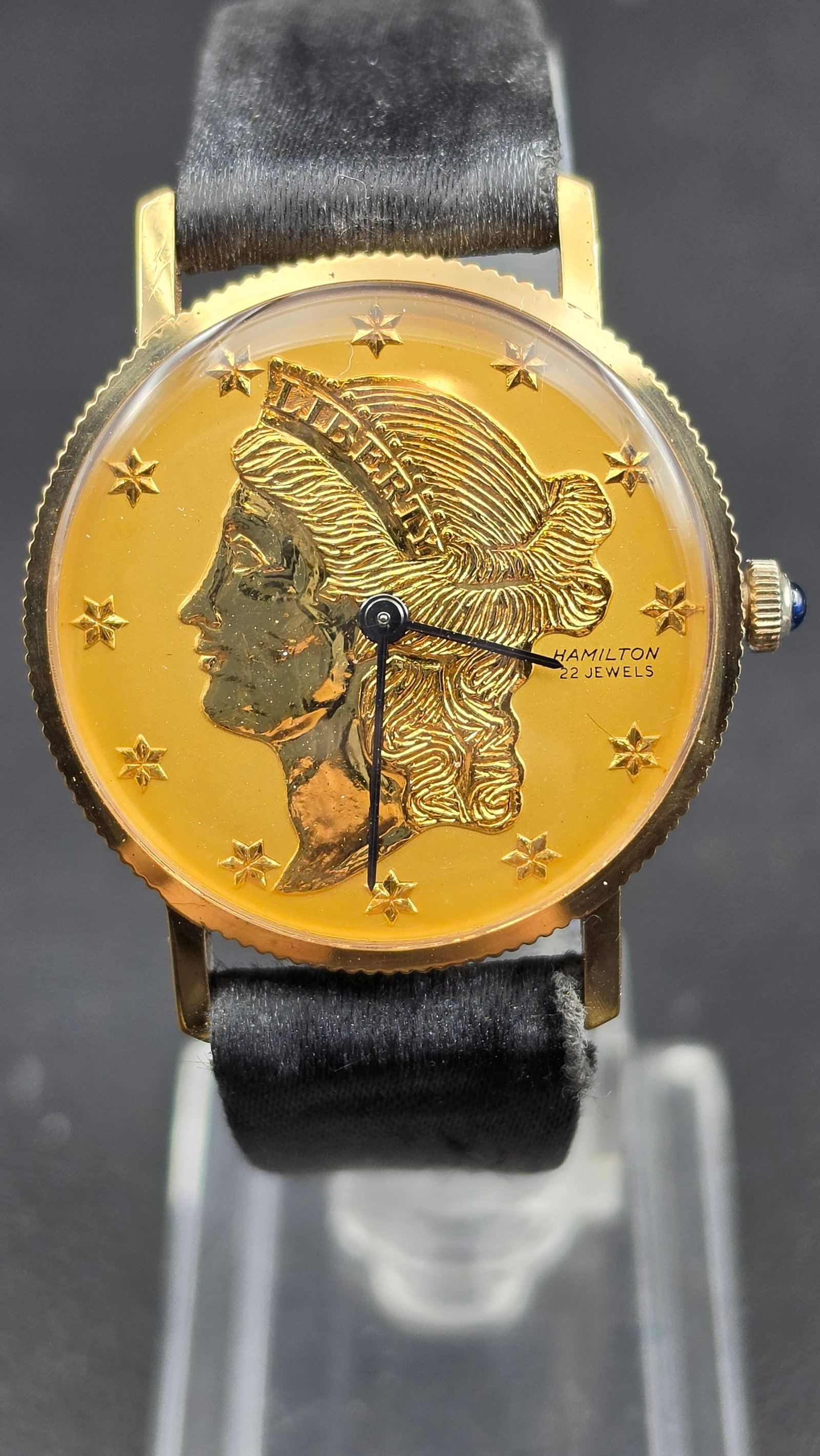 Hamilton Liberty coin watch 22 jewel USA movement 770 gold filled case coin bezel black leather stra: This is a vintage Hamilton Liberty coin style wristwatch. The round case measures 33.34mm and features a deeply knurled coin-edge bezel in gold tone. The inner case back is stamped with what appears t