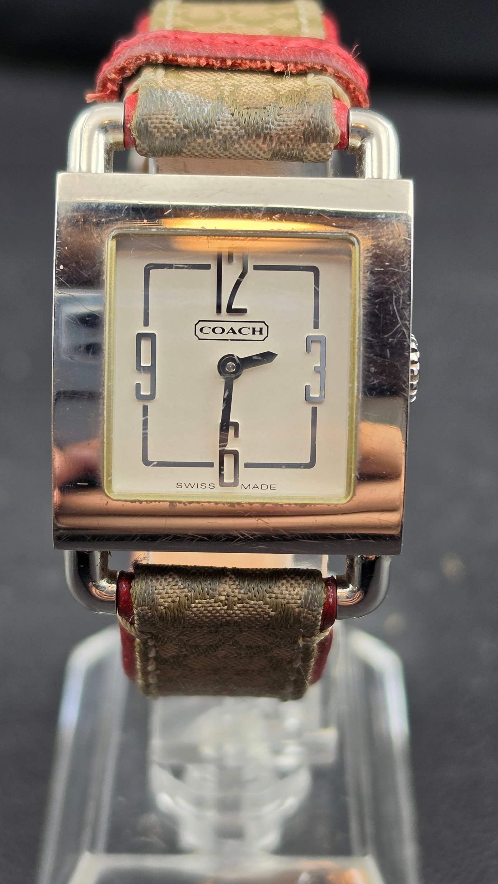 Coach Swiss Made Ladies Quartz Watch 20.51mm 0221 6.681.416 Stainless Steel Signature Strap: White square dial with Coach logo in a cartouche at center, Arabic numerals at 12, 3, 6, and 9 with a decorative square frame graphic, Swiss Made text at the bottom, and gold-tone hands. Square stainl