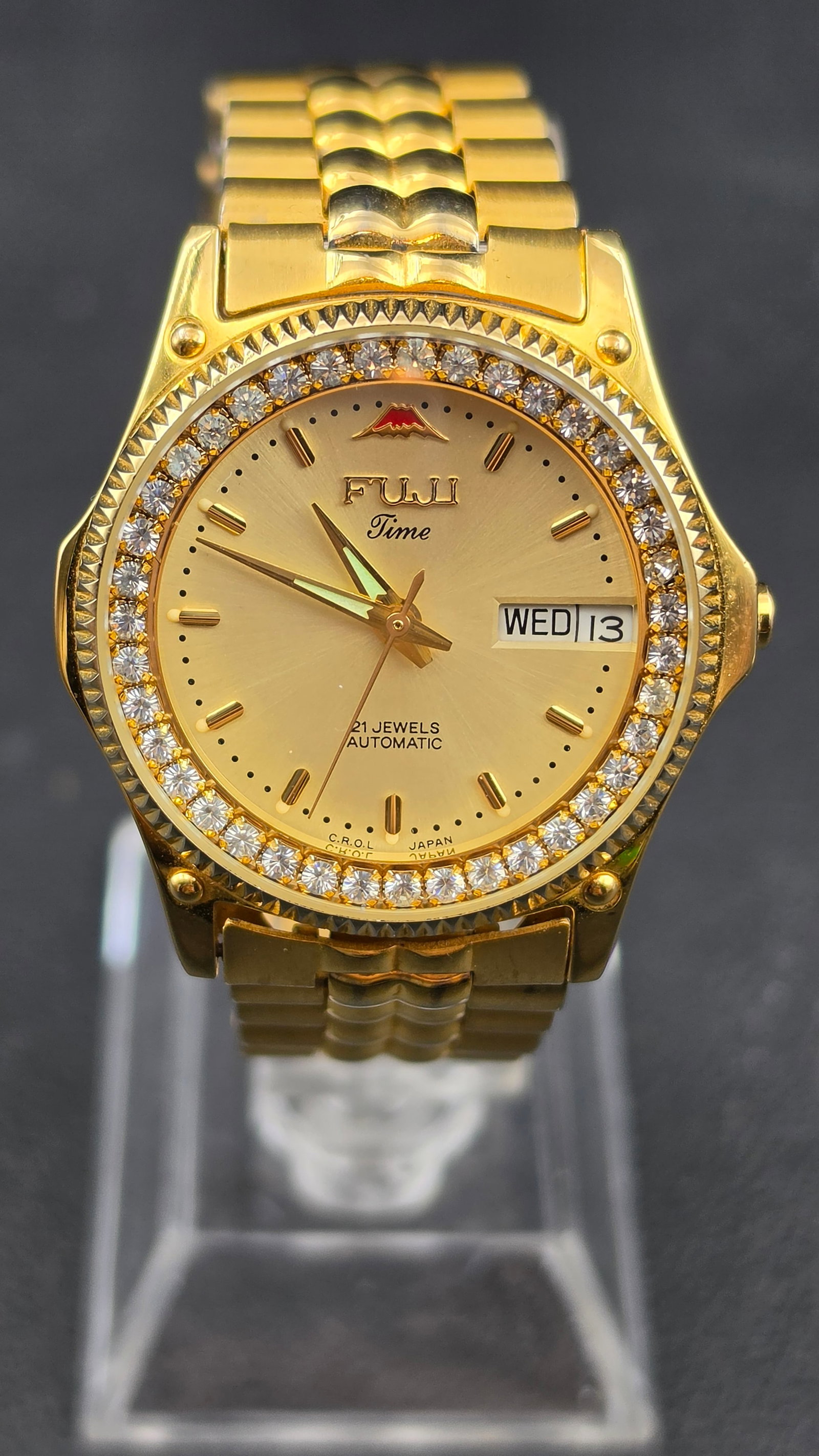 Fuji Time 21 Jewels Automatic Gold Tone Day Date CZ Bezel Watch Japan 32.93mm: Fuji Time automatic wristwatch in gold tone finish. The champagne sunburst dial features applied baton hour markers, no numerals, a day and date window at 3 o'clock displaying WED and 13, and printed 