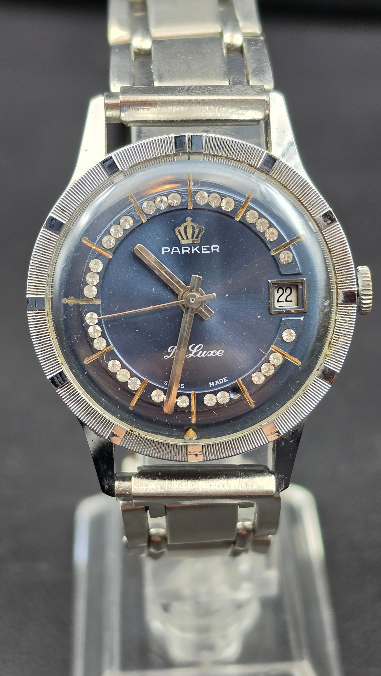Parker De Luxe Swiss Made Blue Dial CZ Stone Ring Date Coin Edge Bezel 34.55mm: Vintage Parker De Luxe Swiss made wristwatch. The blue sunburst dial features gold tone baton hour markers, a full inner ring of CZ rhinestone stones, the Parker crown logo and brand name printed abov