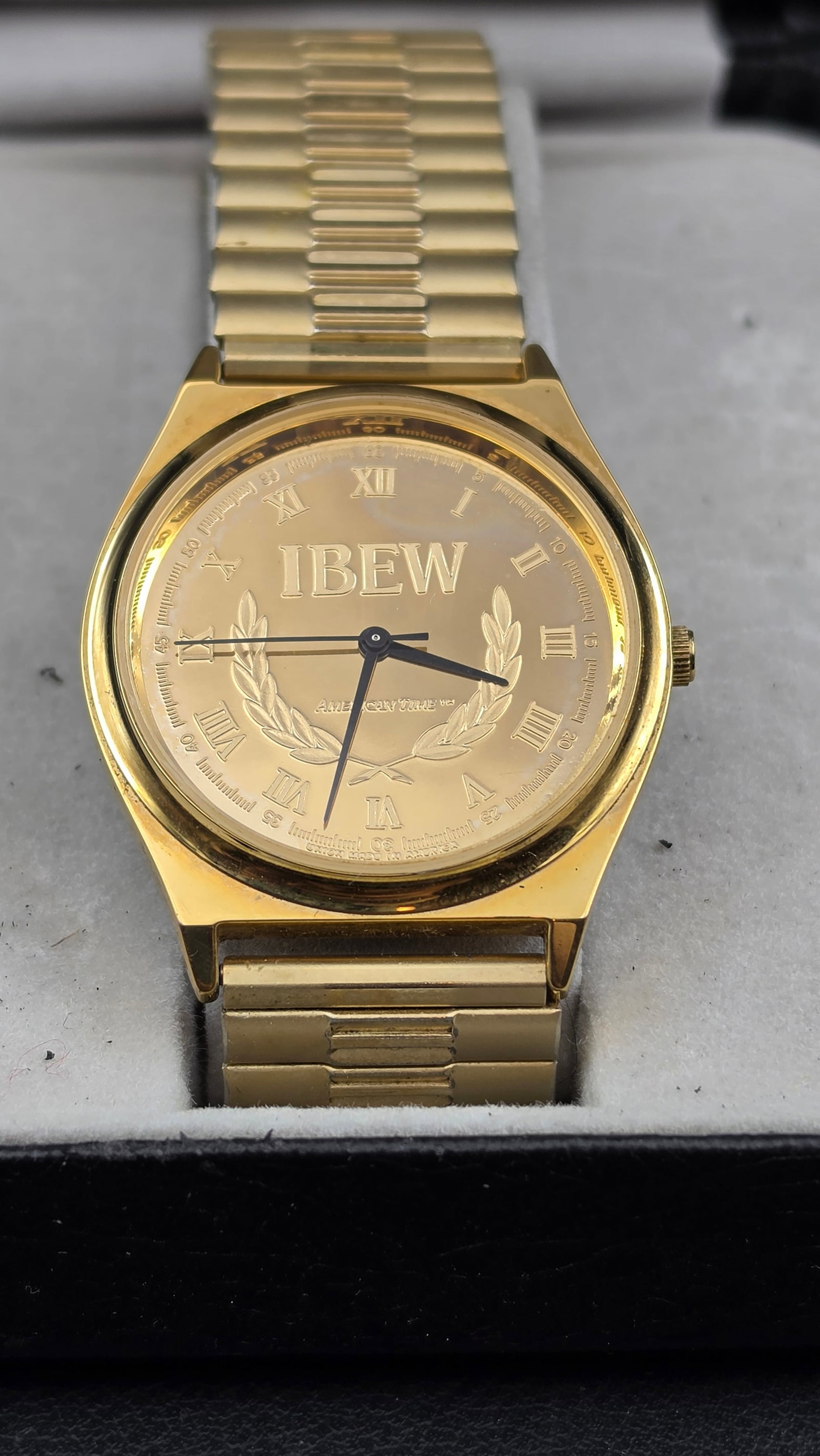 IBEW American Time Quartz Watch 33.97mm Gold Tone Speidel Bracelet Local Union 697 1996 NOS: IBEW International Brotherhood of Electrical Workers quartz wristwatch by American Time, new old stock. Case measures 33.97mm as shown on calipers. Gold tone case with a champagne gold sunburst dial f