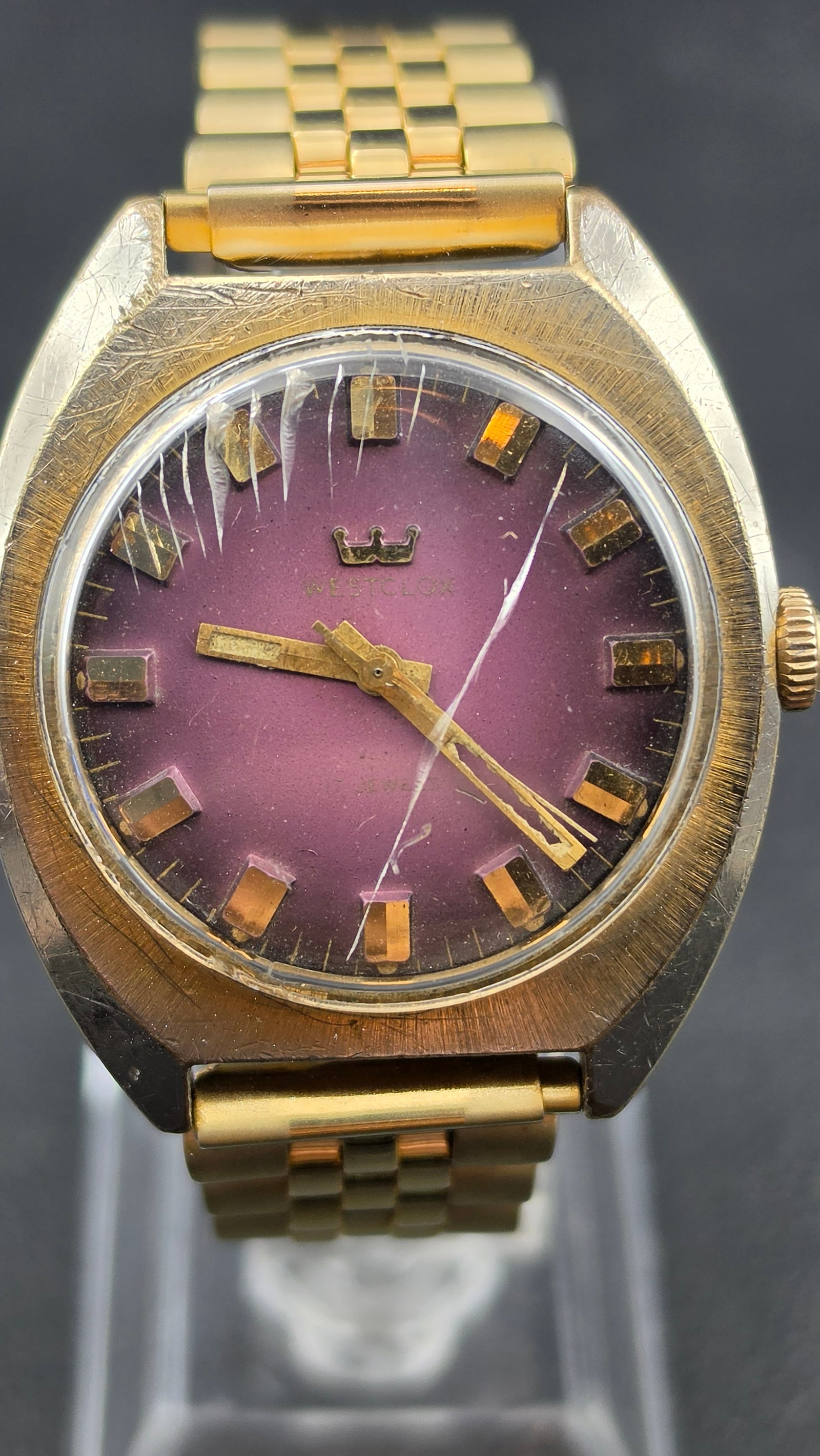 Westclox Purple Dial Gold Tone Watch Jubilee Style Bracelet Base Metal c.1970s 36mm: This is a vintage Westclox manual wind wristwatch featuring a striking purple dial. The purple sunburst gradient dial deepens toward the outer edge and features a gold-toned crown logo above the Westc