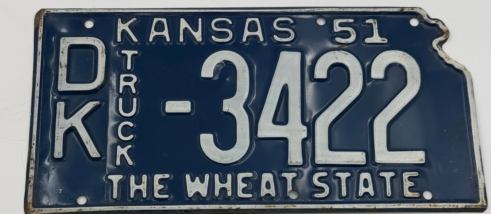 1951 Kansas “The Wheat State” Truck License Plate D-3422: Vintage 1951 Kansas truck license plate featuring “The Wheat State” slogan and embossed white lettering on blue background. Plate number D-3422. Made of metal with original patina and wear fro