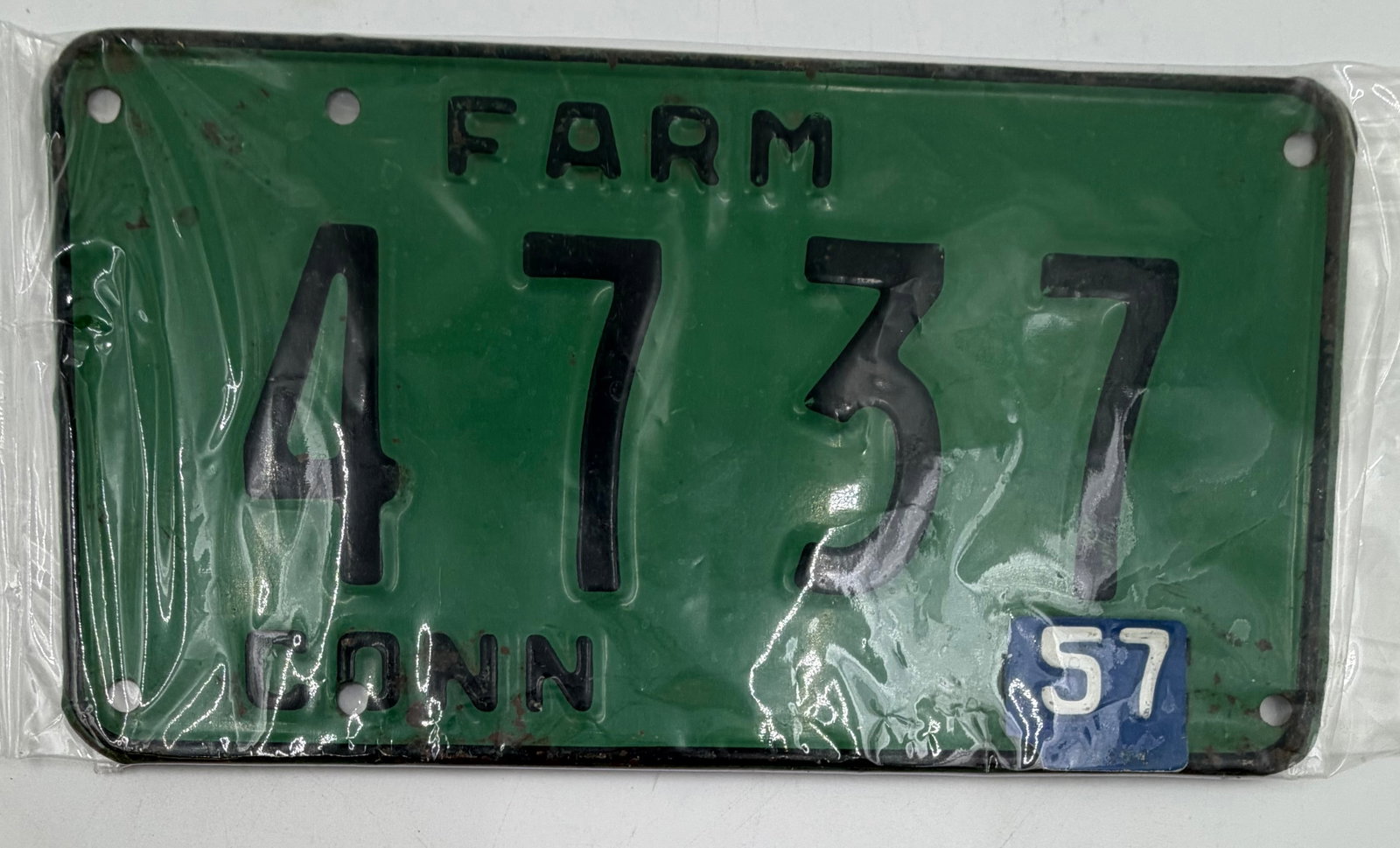 1957 Connecticut Farm License Plate 4737: Original 1957 Connecticut FARM license plate, number 4737, featuring green background with black embossed numbers and blue “57” validation tab. Stored in protective plastic sleeve. Shows light
