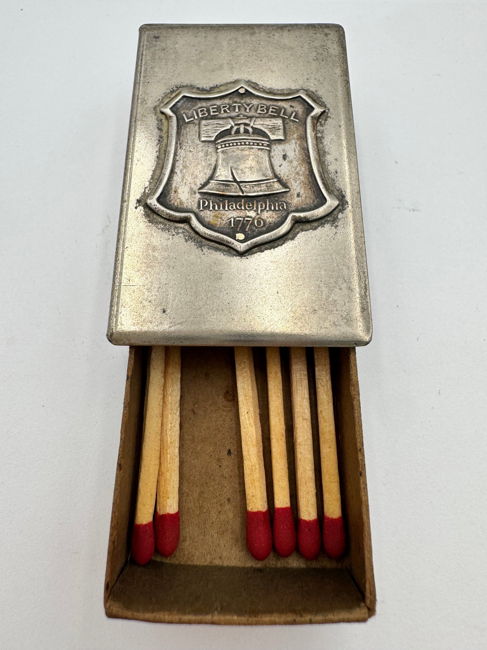 Vintage Liberty Bell Philadelphia 1776 Souvenir Match Holder Vesta Case: Vintage Liberty Bell themed metal match holder or vesta case featuring an embossed Liberty Bell emblem marked “Philadelphia 1776.” Sliding drawer design with wooden interior compartment for st