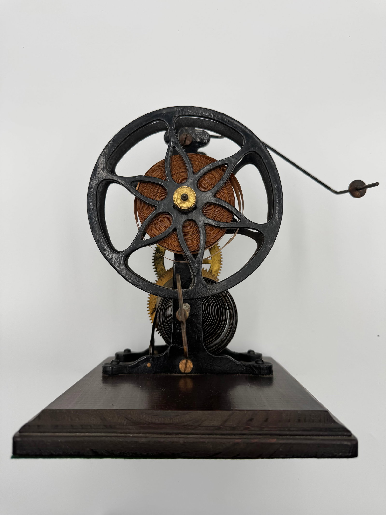 Antique Clockwork Scientific Demonstration Machine: Antique clockwork mechanical demonstration apparatus featuring exposed brass gears, cast iron frame, flywheel, and winding key mounted on a polished wood base. Likely used in a school or laboratory fo