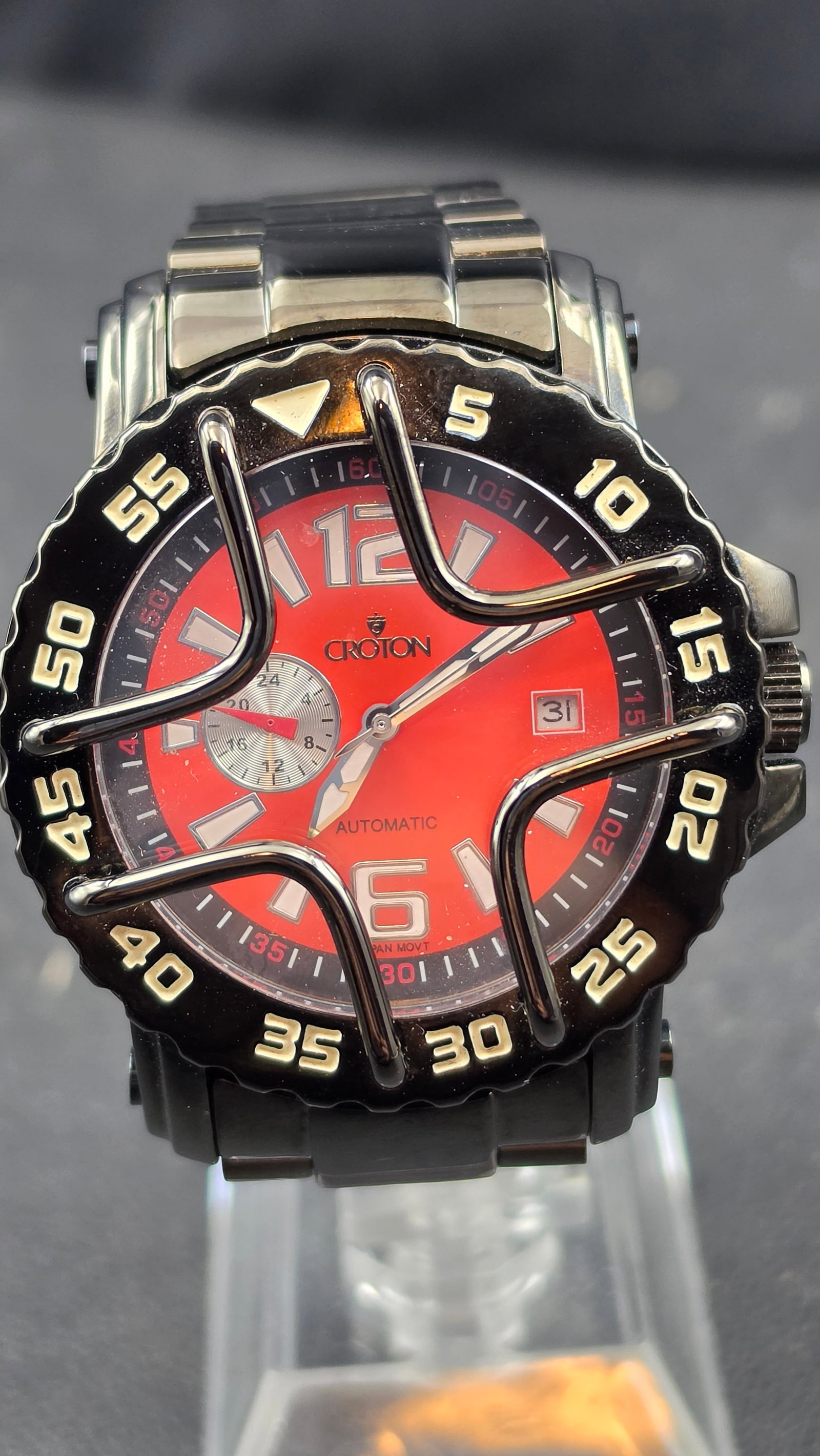 Croton CA301185BKGR Automatic Japan Movement Red Dial Black Ion Plated Skeleton Caseback 44mm 2010: This is a Croton automatic sport diver, reference CA301185BKGR, driven by a Japanese automatic movement visible through a skeleton exhibition caseback. The 43.65mm black ion-plated all stainless steel