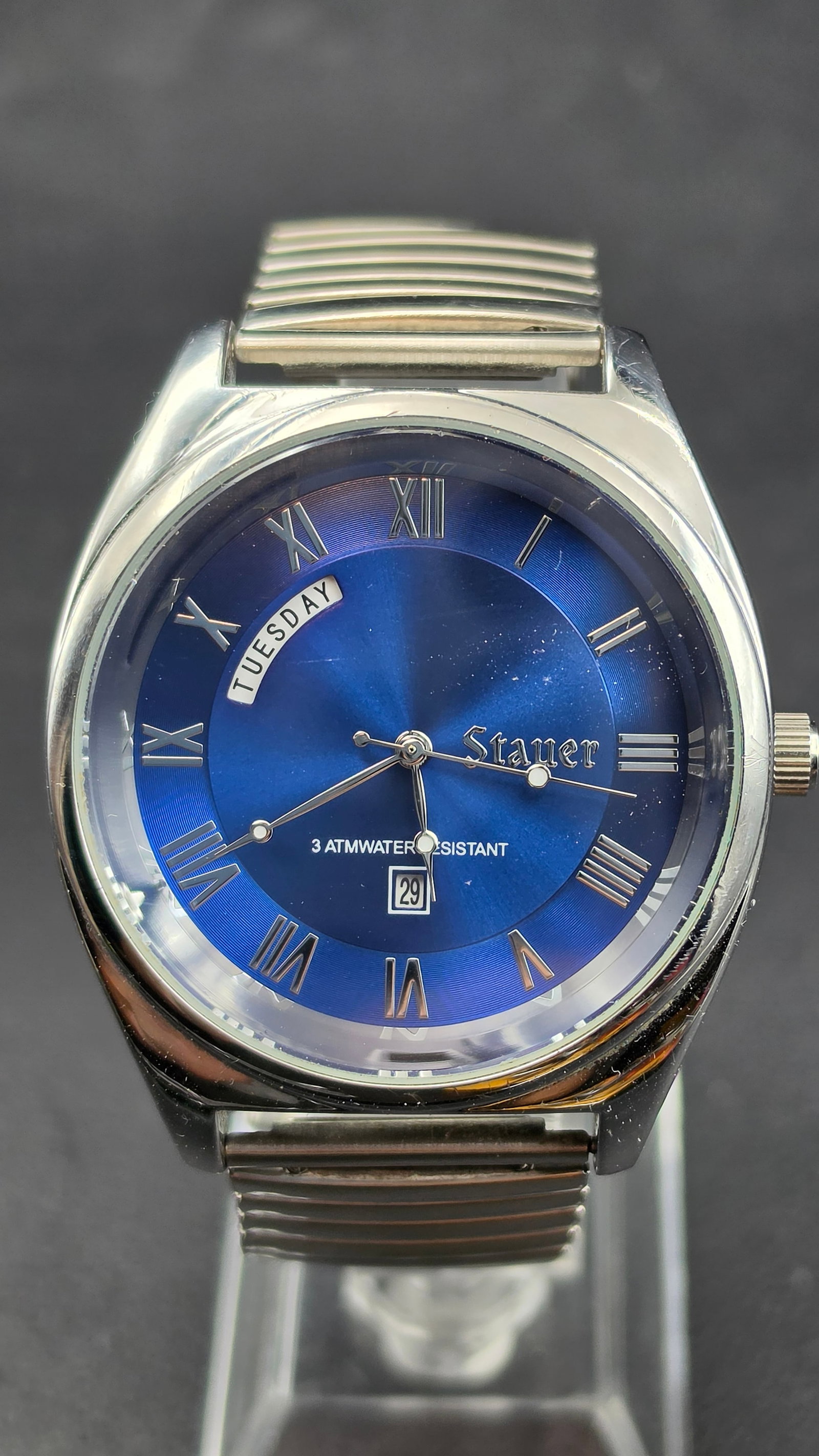 Stauer 43477 Blue Sunburst Dial Day-Date Roman Numeral Japan Movement 42mm Watch 2000s: This is a Stauer reference 43477 featuring a vivid blue sunburst dial with silver Roman numerals, a day window at 10 o'clock displaying the full day name, a date window at 6 o'clock, and the dial sign