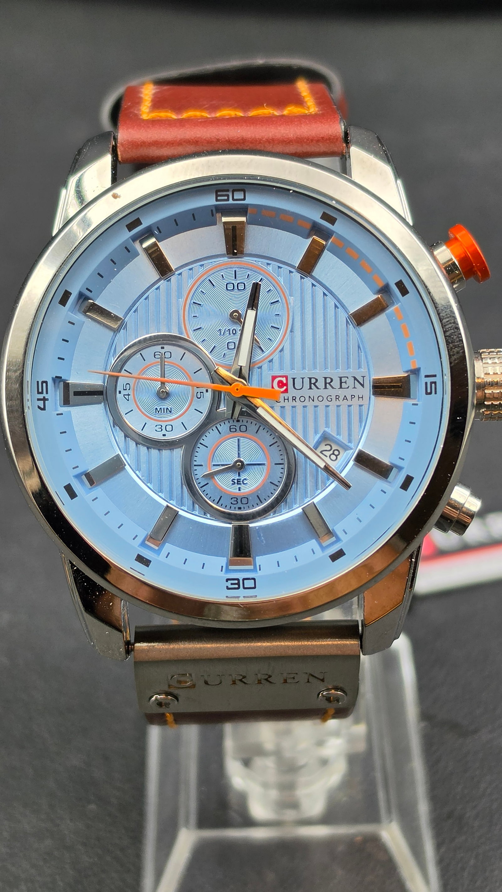 Curren M8291 Chronograph Blue Dial Orange Accent Brown Leather Strap 48mm Watch NOS with Tag 2010s: This is the Curren M8291, a bold oversized chronograph presented new old stock with the original hang tag still attached. The blue textured dial features three subdials — a minutes counter at 9 o'cl