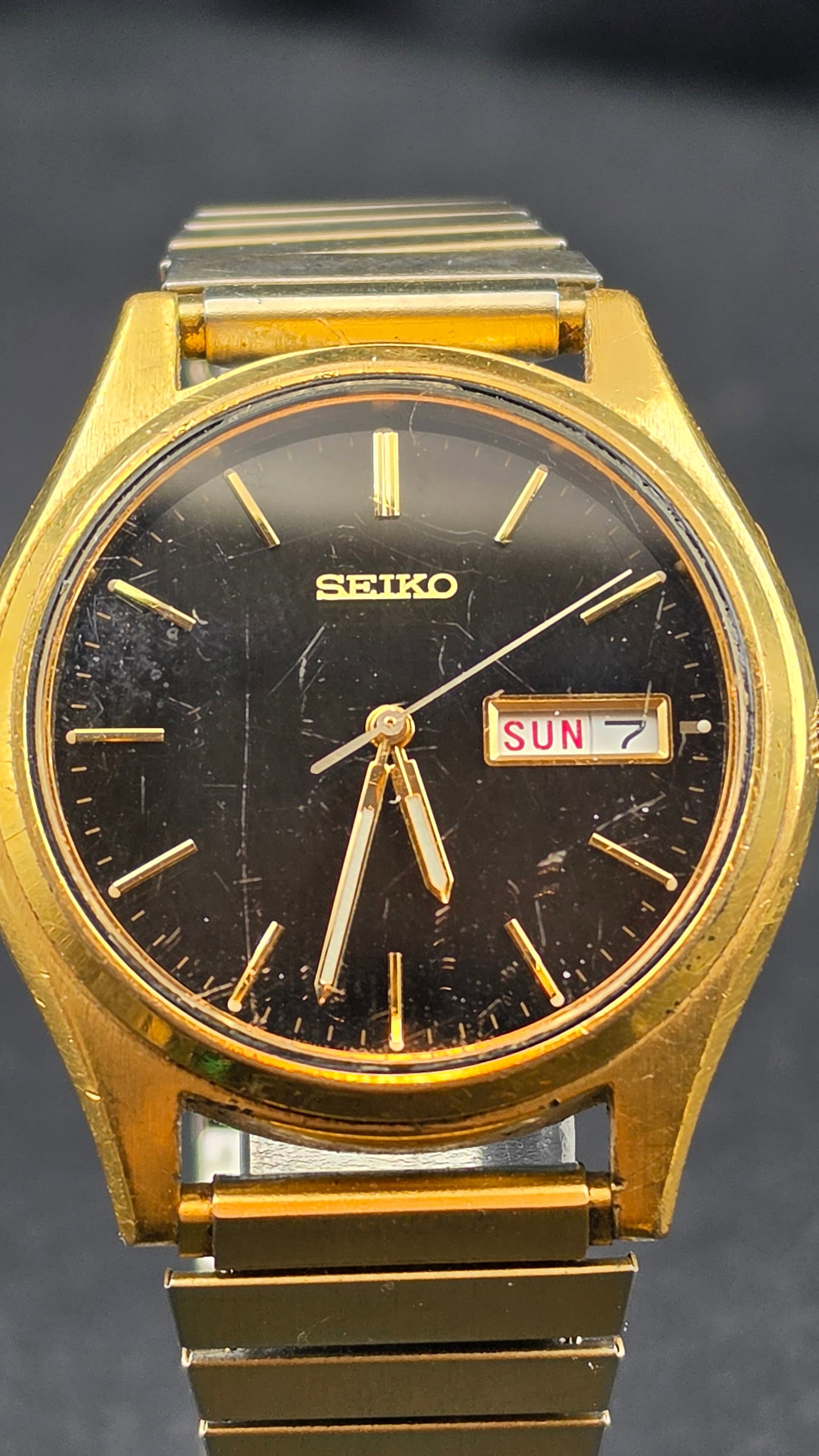 Seiko 7N43-9048 Black Dial Day-Date Gold Tone Quartz 37mm Men's Dress Watch 1980s: This is a vintage Seiko reference 7N43-9048, a classic men's day-date quartz dress watch featuring a black dial with applied gold-tone bar indices, slim gold-tone dauphine hands, and a dual-window day