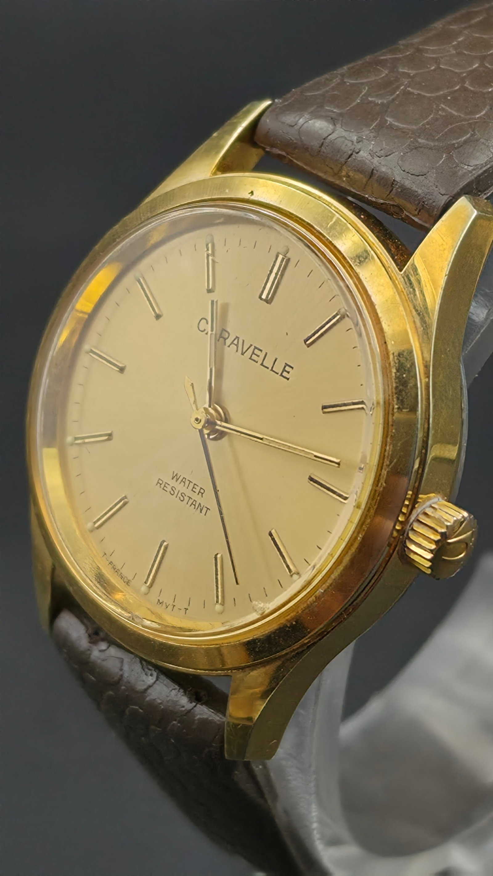 Caravelle by Bulova Manual Wind Gold-Tone Men's Dress Watch 31mm Water Resistant, ca. 1970s, Running: This is a Caravelle by Bulova manual-wind dress watch featuring a champagne sunburst dial with applied gold-tone baton hour markers, gold-tone hands with a sweep seconds hand, and dial text reading "C