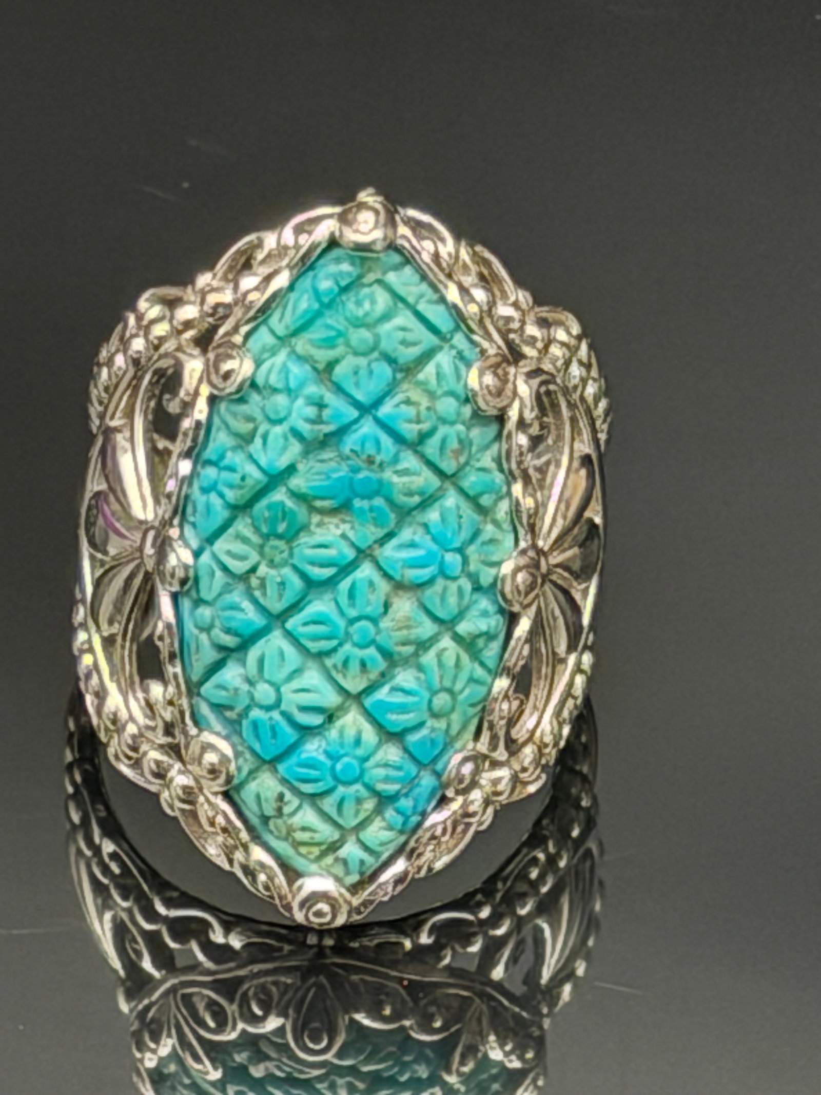 11g-Vintage DP Sterling Silver Carved Turquoise Floral Statement Ring: Vintage artisan sterling silver statement ring featuring an intricately hand-carved turquoise gemstone with floral and lattice motifs. The large shield-shaped turquoise centerpiece is set in an elabor