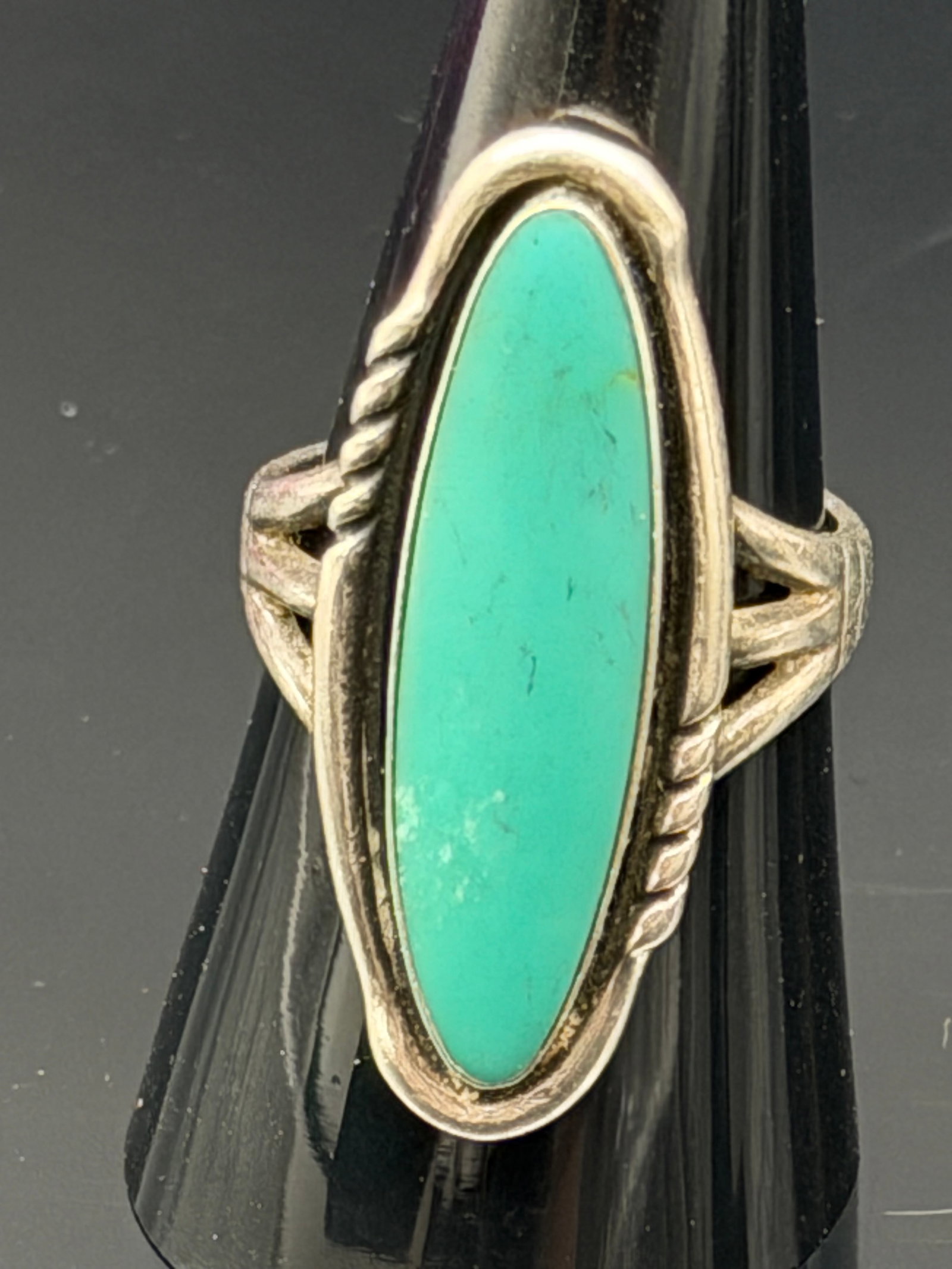 7g- Vintage Sterling Silver Turquoise Navette Ring: Vintage sterling silver ring featuring a large elongated turquoise cabochon in a sleek navette setting. The ring is accented with twisted silver wire details and a split-shank band, giving it a classi