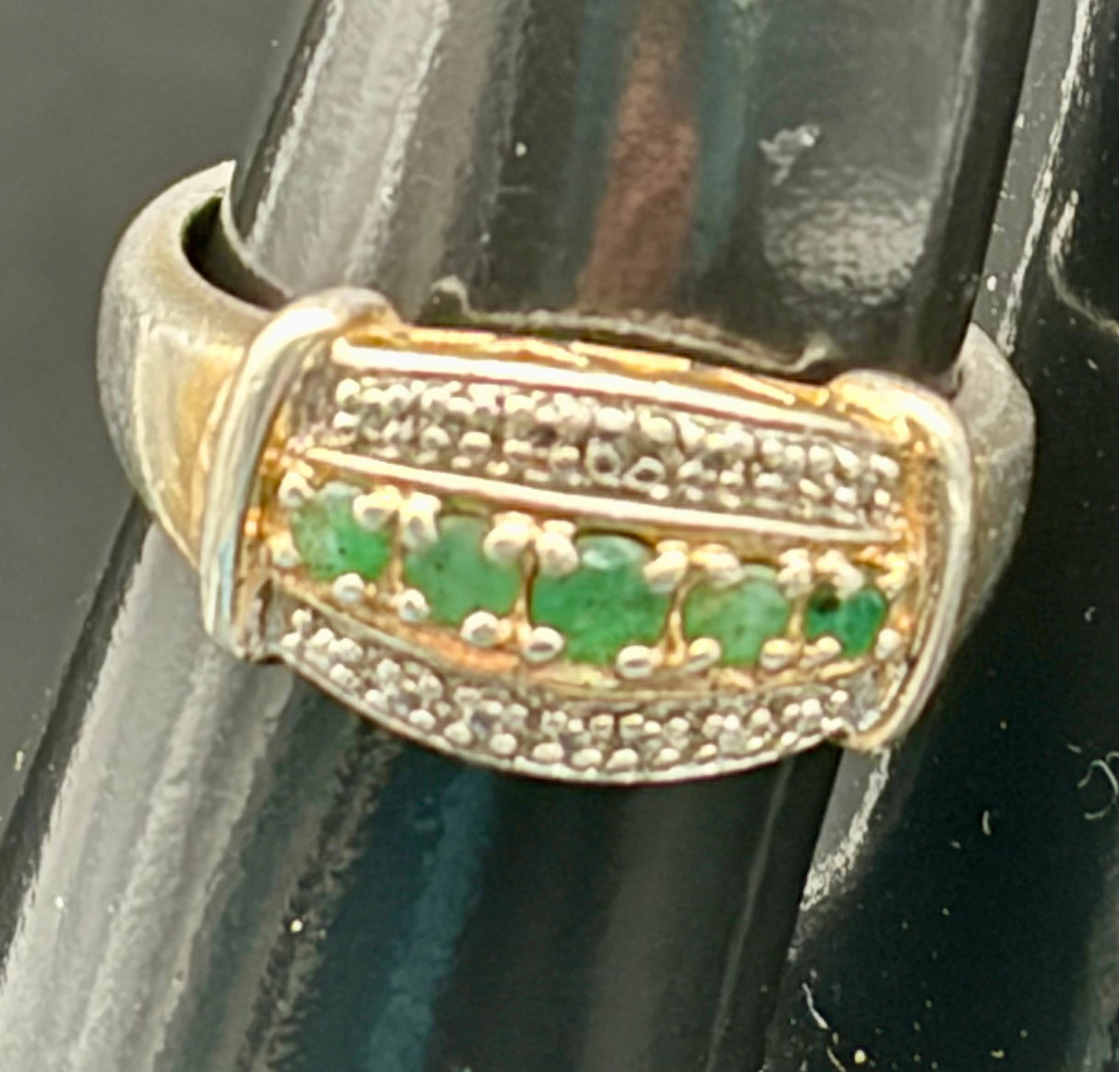 4.1g 925 Sterling Silver Emerald CZ Ring China: Elegant sterling silver ring featuring a row of green stones, likely simulated emeralds, accented by sparkling clear stones. Marked 925 and CHINA, weighing 4.1 grams. The ring has a two-tone appearanc