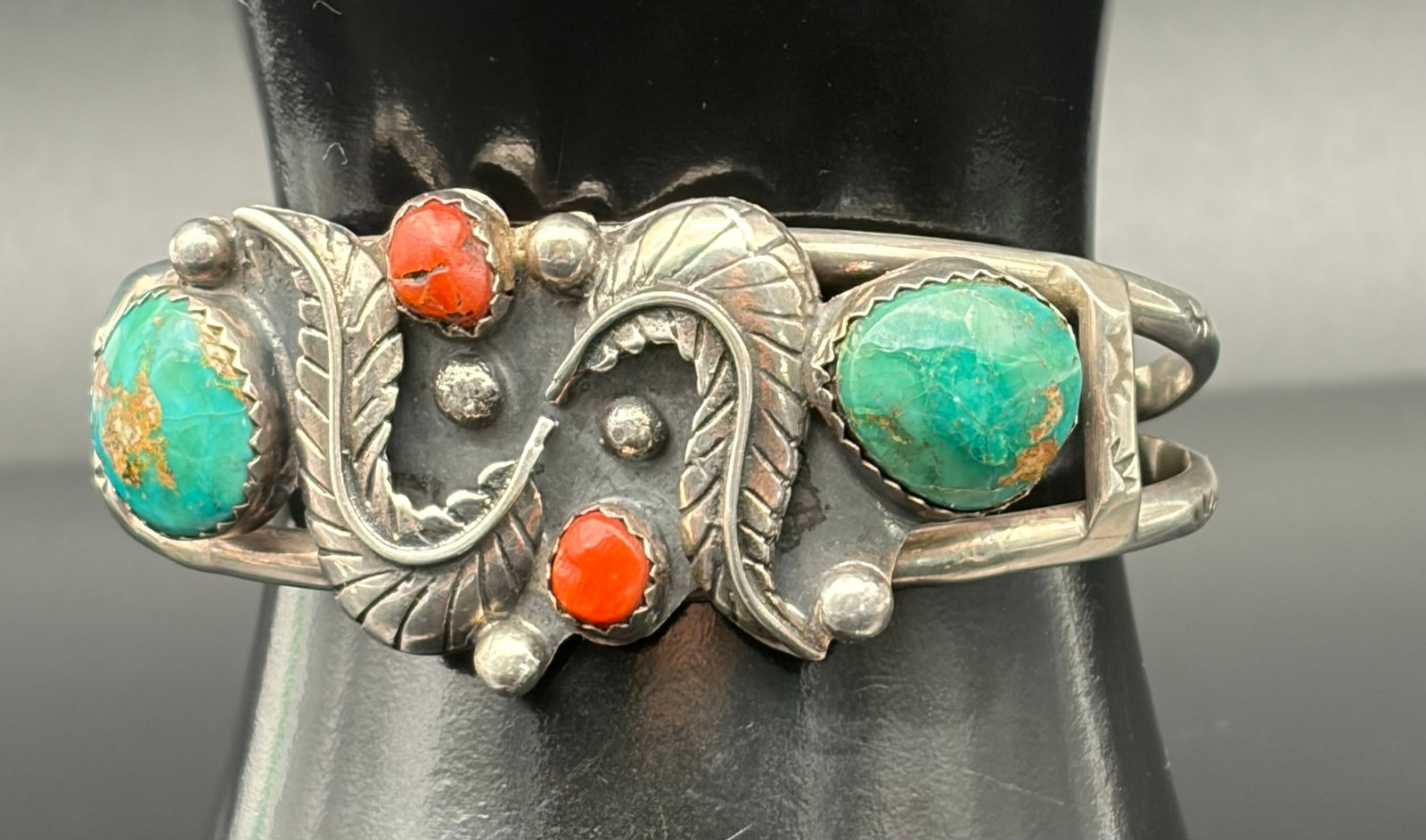 26.4g Vintage Sterling Silver Turquoise Coral Cuff Bracelet: Vintage sterling silver cuff bracelet weighing 26.4 grams. Features two turquoise cabochons and two coral stones set within a hand-crafted leaf and vine design. Oxidized finish highlights the detailed