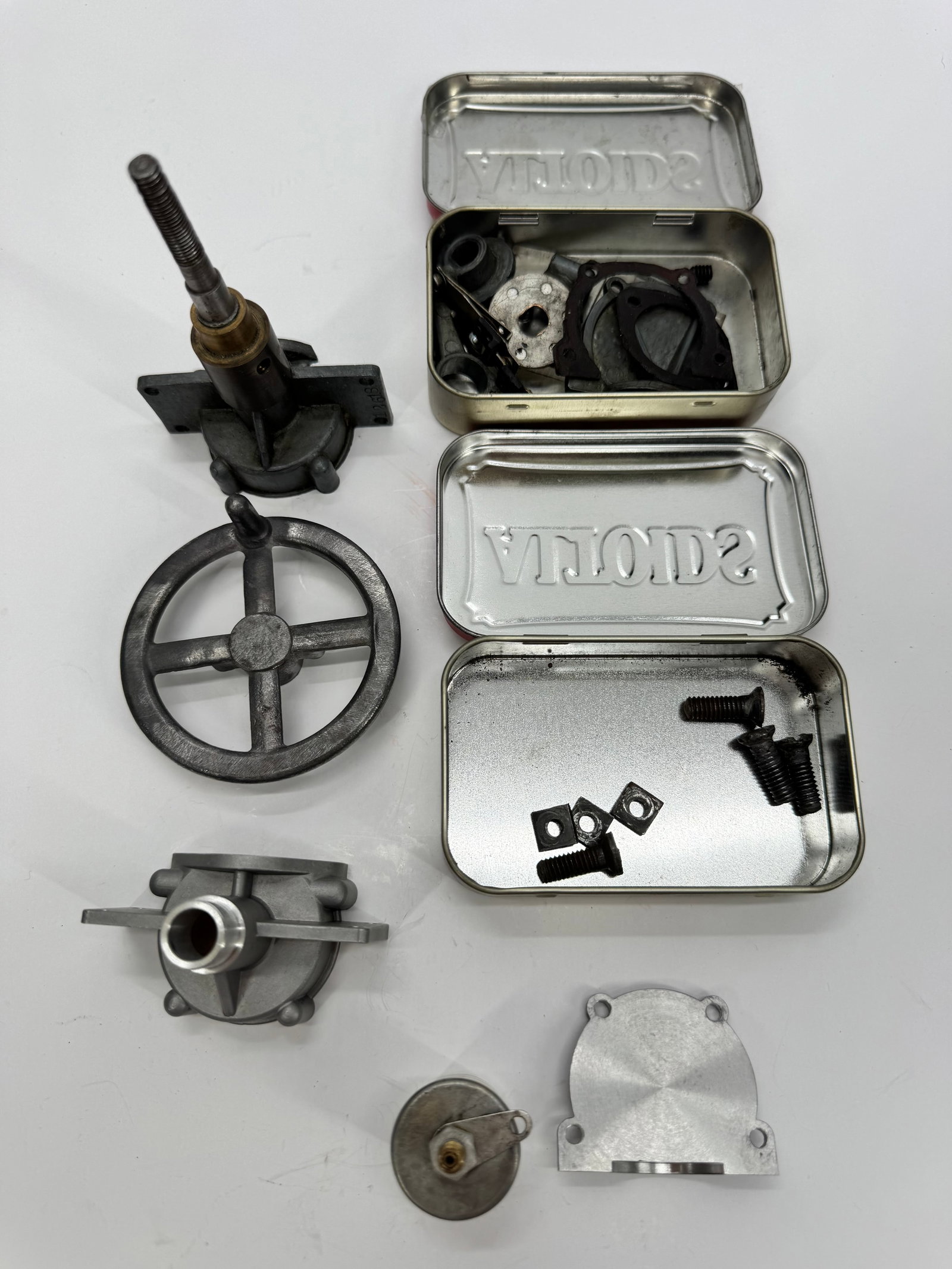 Sky Chief Outboard Motor Parts Lot in Solola Tobacco Tin: Collection of vintage Sky Chief outboard motor parts and components housed in a Solola tobacco tin. Includes various cast metal fittings, mounting pieces, gaskets, hardware, and mechanical components 