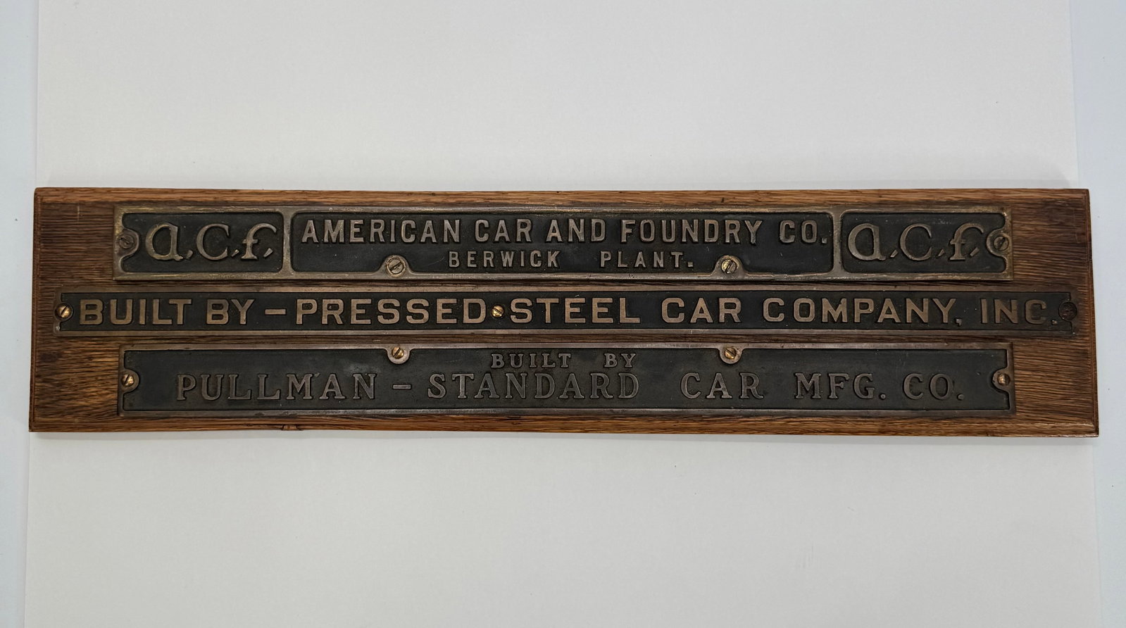 Railroad Builder Plate Display – ACF, Pullman & Pressed Steel: Decorative wall-mounted display featuring reproduction or salvaged-style railroad builder plates representing American Car & Foundry (ACF), Pressed Steel Car Company, and Pullman-Standard Car Manufact