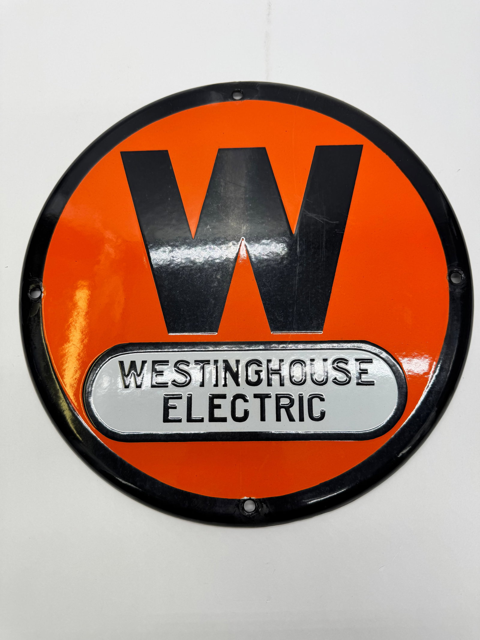 Vintage Westinghouse Electric Porcelain Enamel Sign: Vintage Westinghouse Electric porcelain enamel advertising sign featuring the iconic orange-and-black “W” logo. Approx. 12” diameter with original mounting holes and strong gloss. Displa