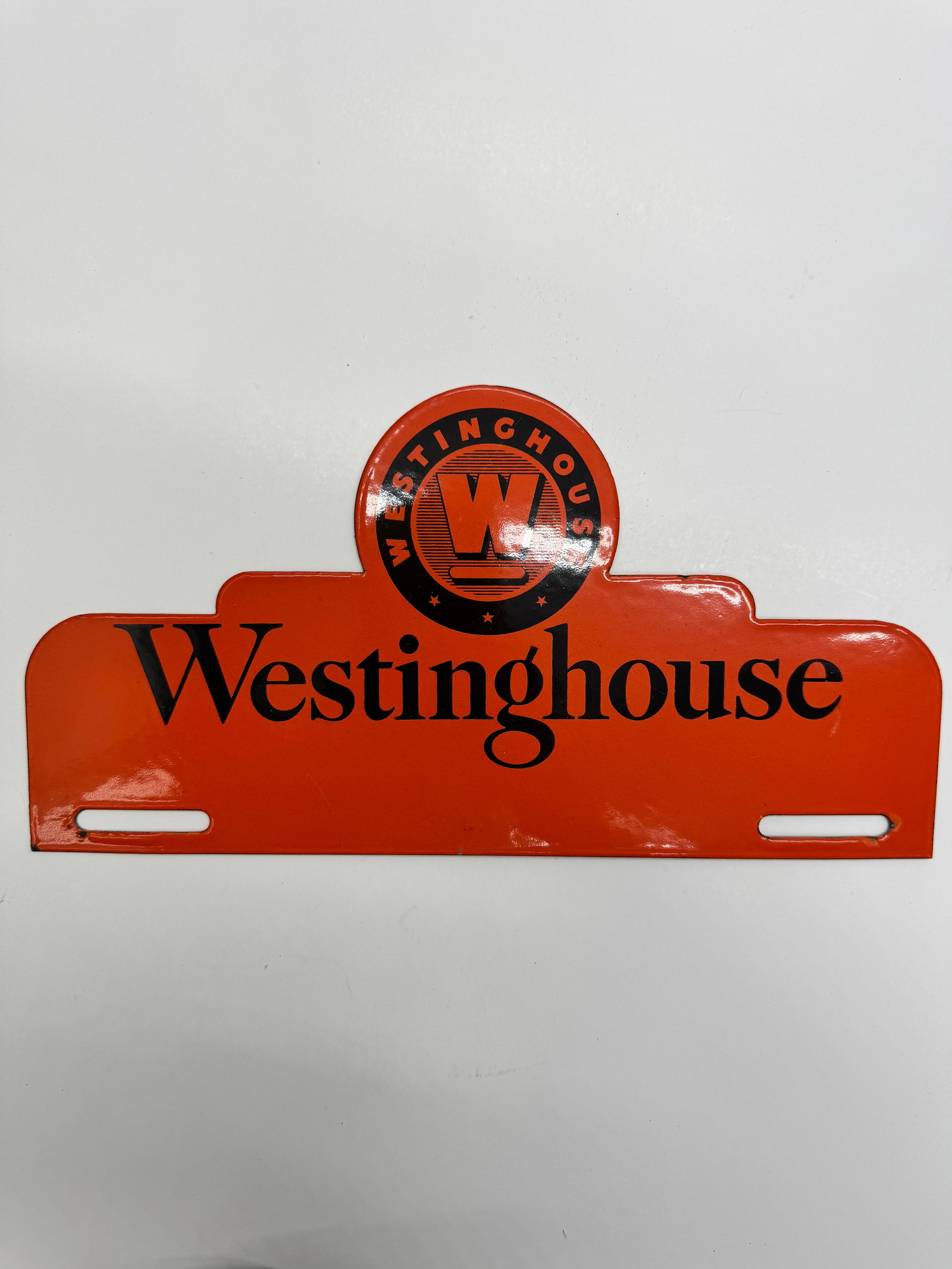 Vintage Westinghouse Electric License Plate Topper: Original embossed steel Westinghouse Electric license plate topper featuring the early circular “W” logo on a bright orange background. Displays beautifully with minor age-related wear. A desi