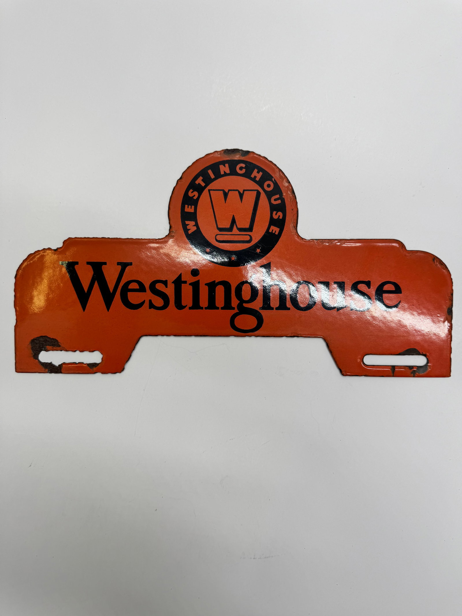Vintage Westinghouse Electric License Plate Topper: Westinghouse Electric license plate topper featuring the early circular “W” logo on an orange background. Shows paint loss, edge wear, and age-related use, but remains a desirable piece of Wes