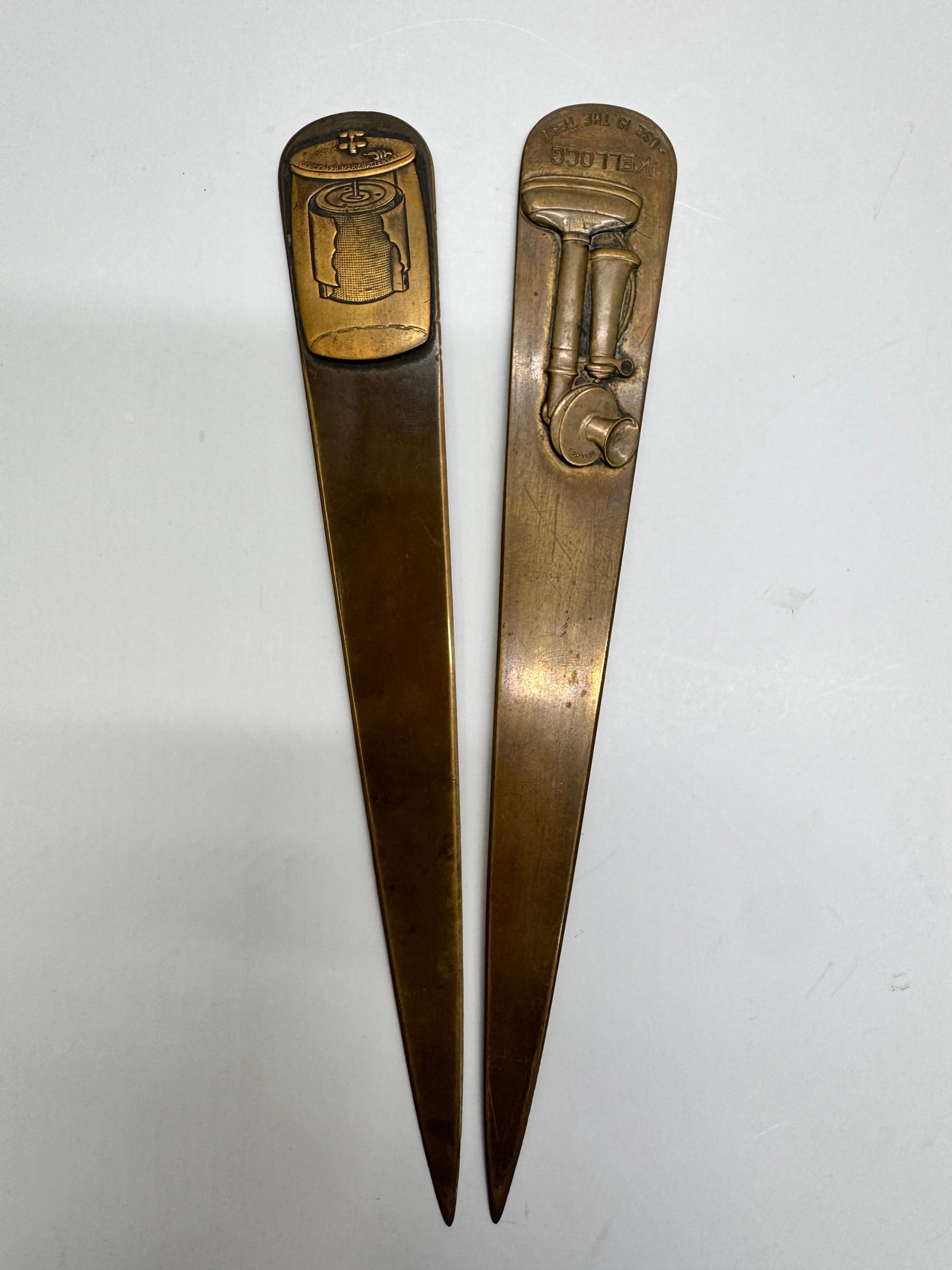 Pair Antique Brass Advertising Letter Openers – Gordon Battery & Kellogg: Pair of antique embossed brass advertising letter openers featuring early electrical and telephone industry advertising. One depicts a Gordon Primary Battery Co. dry-cell battery, while the other feat