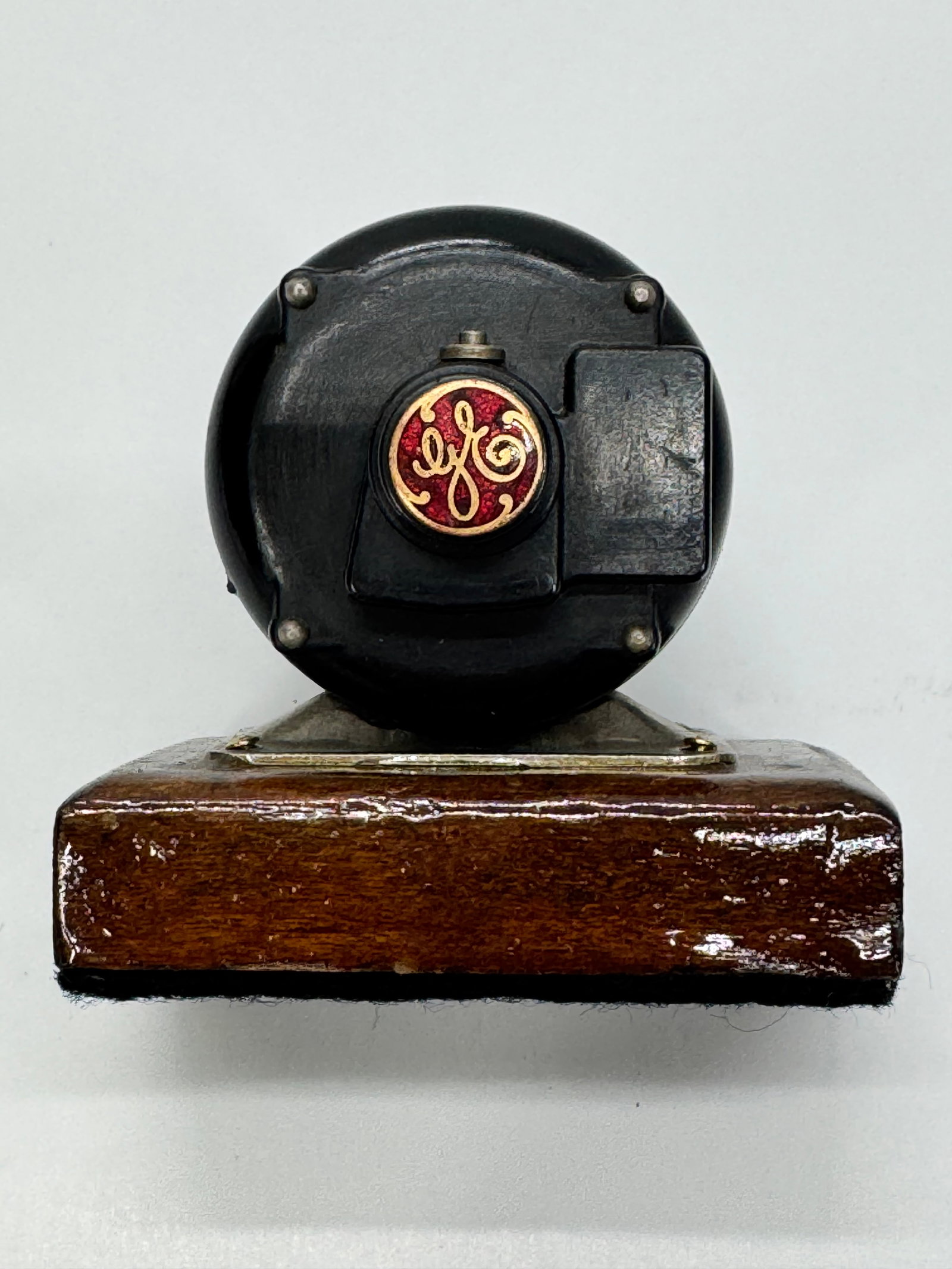 Vintage GE Electric Motor Paperweight on Wood Base: Vintage General Electric (GE) cast metal electric motor paperweight mounted on its original wooden display base. Features the classic red-and-gold GE emblem, dual shaft design, and black painted finis