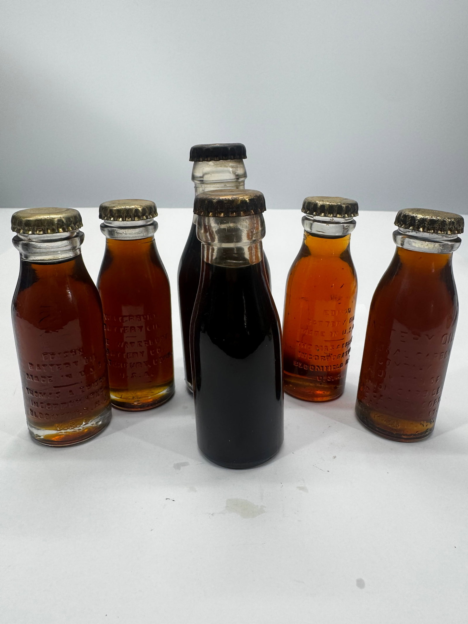 Lot of 5 Antique Edison Battery Oil Glass Bottles w/ Original Caps: Lot of five antique Edison Battery Oil glass bottles in assorted sizes, including embossed examples from Thomas A. Edison and Edison Battery Oil. Most retain their original metal crown caps, with one 