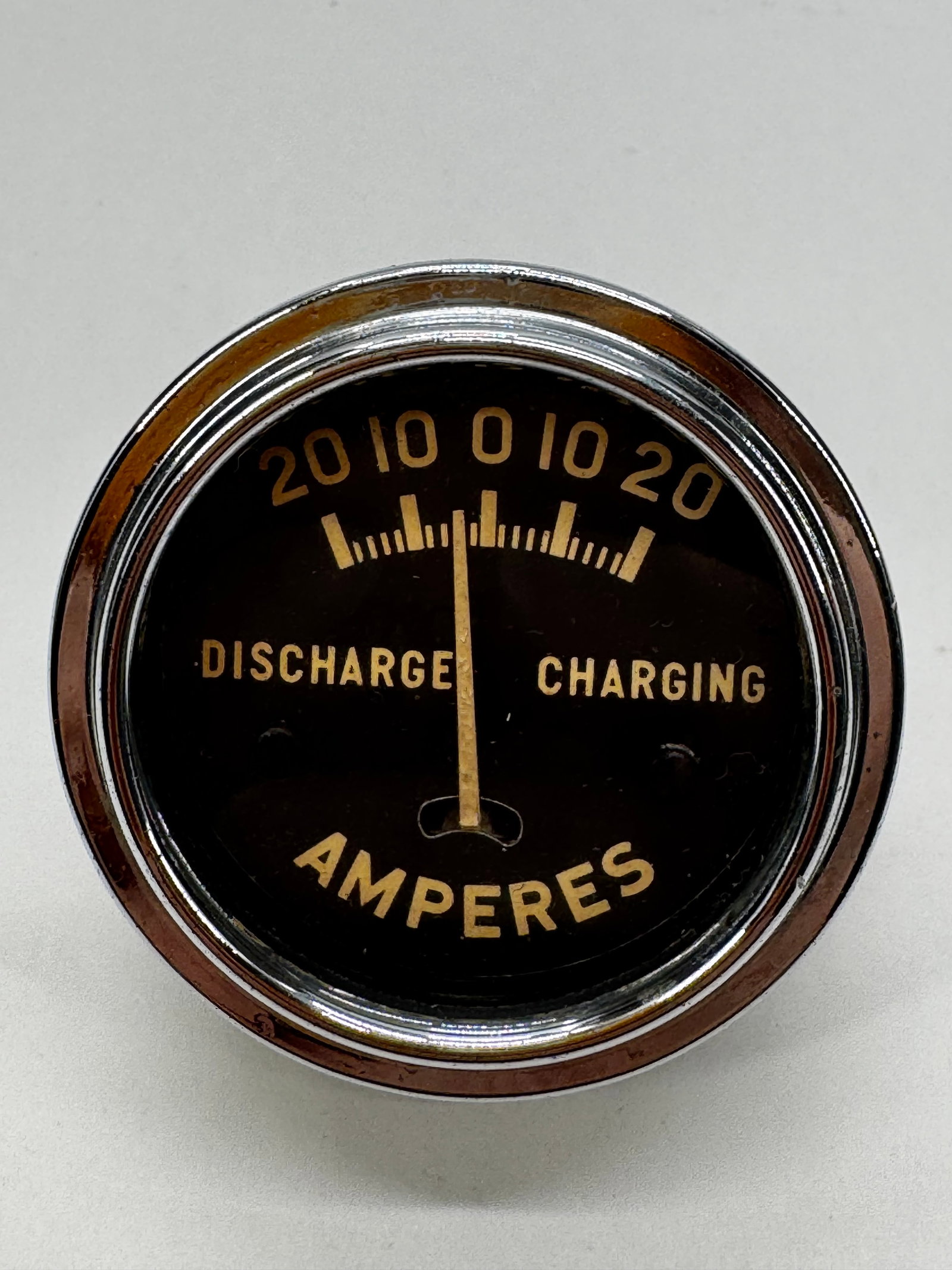 Vintage 20-0-20 Ampere Charge Discharge Gauge Meter: Vintage automotive 20-0-20 ampere charge/discharge gauge featuring a black dial with gold lettering and chrome bezel. Designed to indicate battery charging and discharging current, this gauge was comm