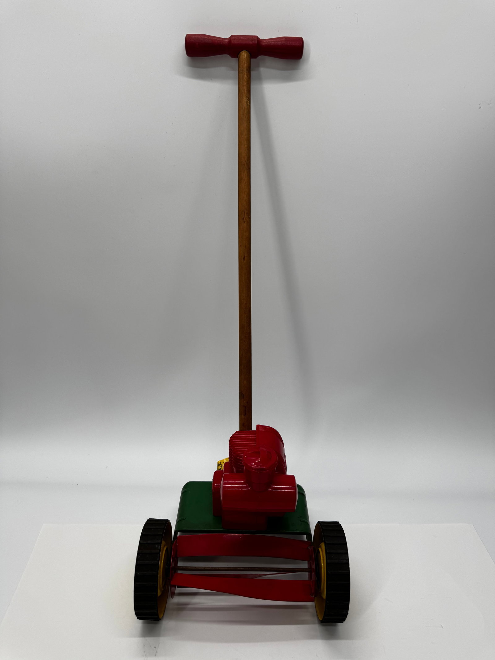 Vintage Toy Push Reel Lawn Mower: Vintage toy push reel lawn mower with red and green plastic body, wooden handle, and rolling wheels with rotating reel blades. Embossed “W” logo on the engine cover. A fun mid-century children