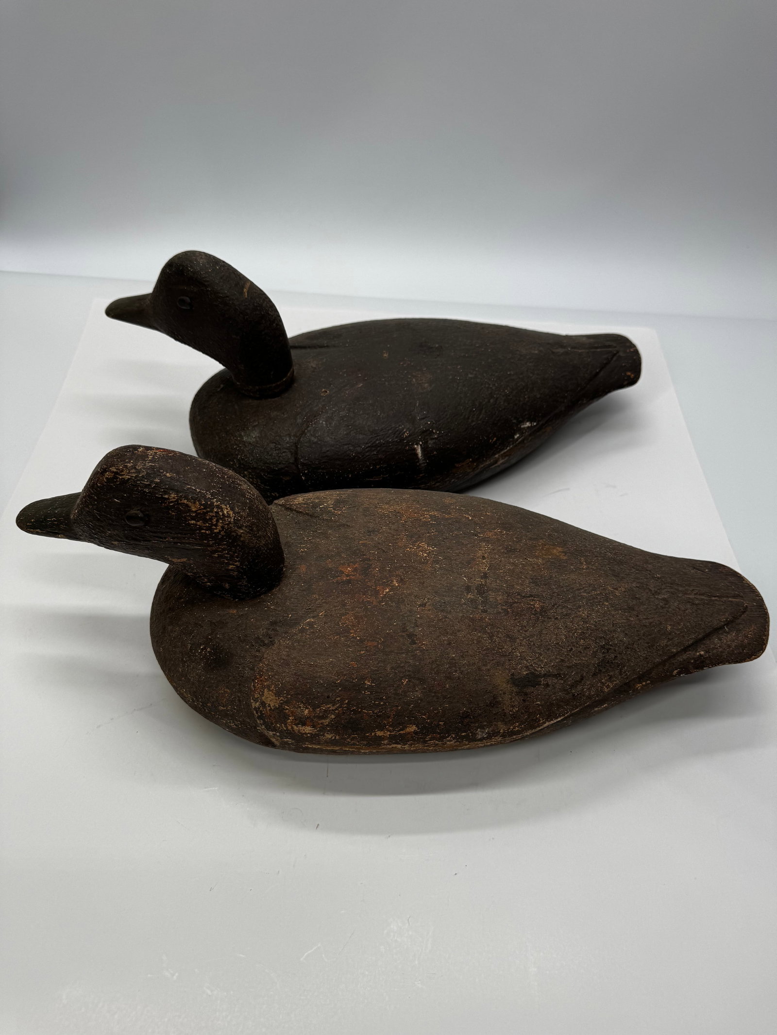 Antique Hand Carved Wooden Duck Decoys Pair: Pair of antique hand-carved wooden duck decoys with original dark painted finish. Solid wood construction featuring carved heads, painted eyes, and hand-shaped bodies. Both display authentic age, wear