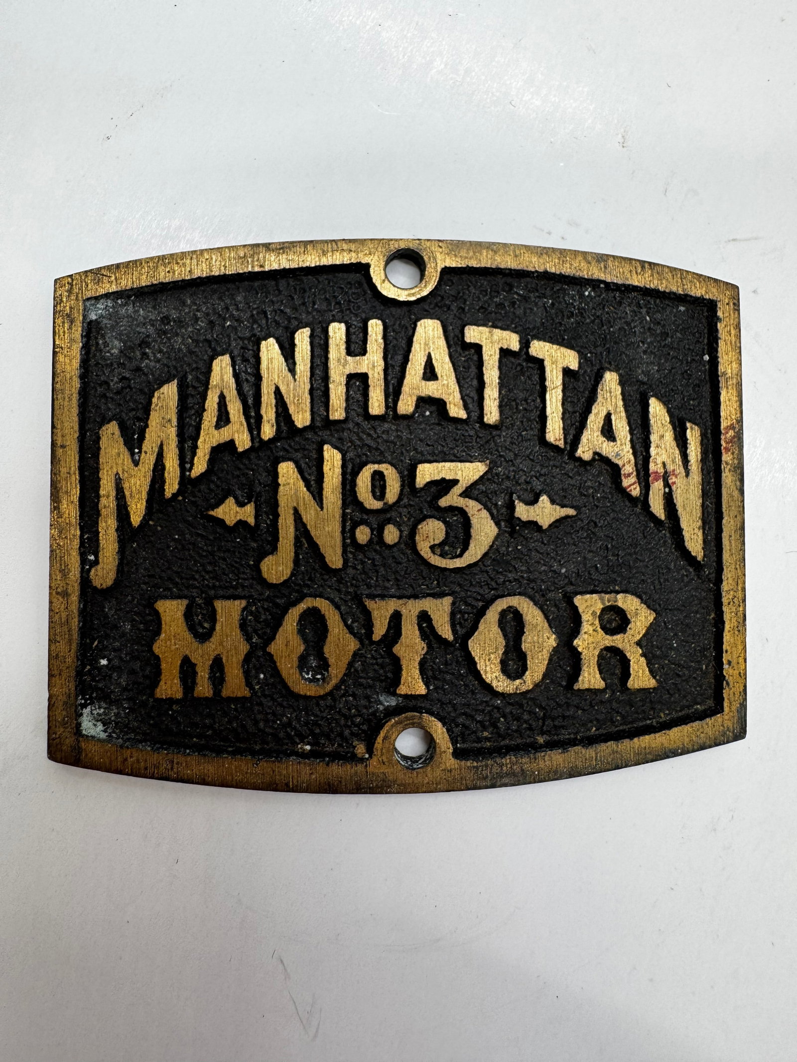 Vintage Manhattan No. 3 Electric Fan Motor Nameplate Tag: Original vintage Manhattan No. 3 Motor identification nameplate from an early electric fan. This curved metal tag features raised gold lettering on a black background reading “MANHATTAN No. 3 MOTOR.