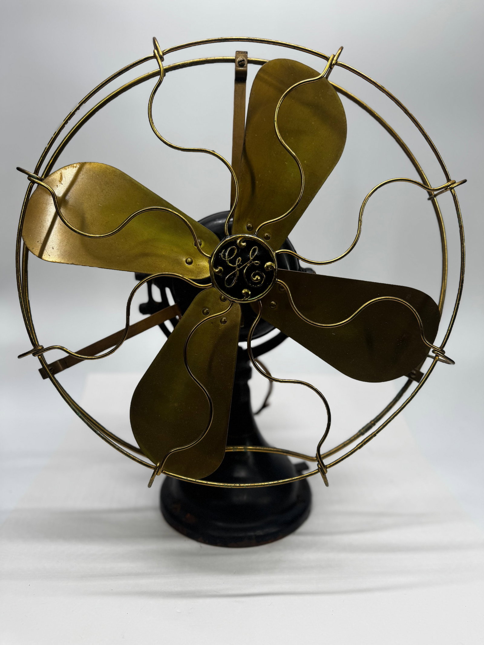 Antique General Electric GE Brass Blade Oscillating Electric Fan c. 1901–1910: Antique General Electric (GE) oscillating electric desk fan dating to the early 1900s. This fan features a heavy cast iron base and motor housing, four original brass blades, an ornate GE center hub, 