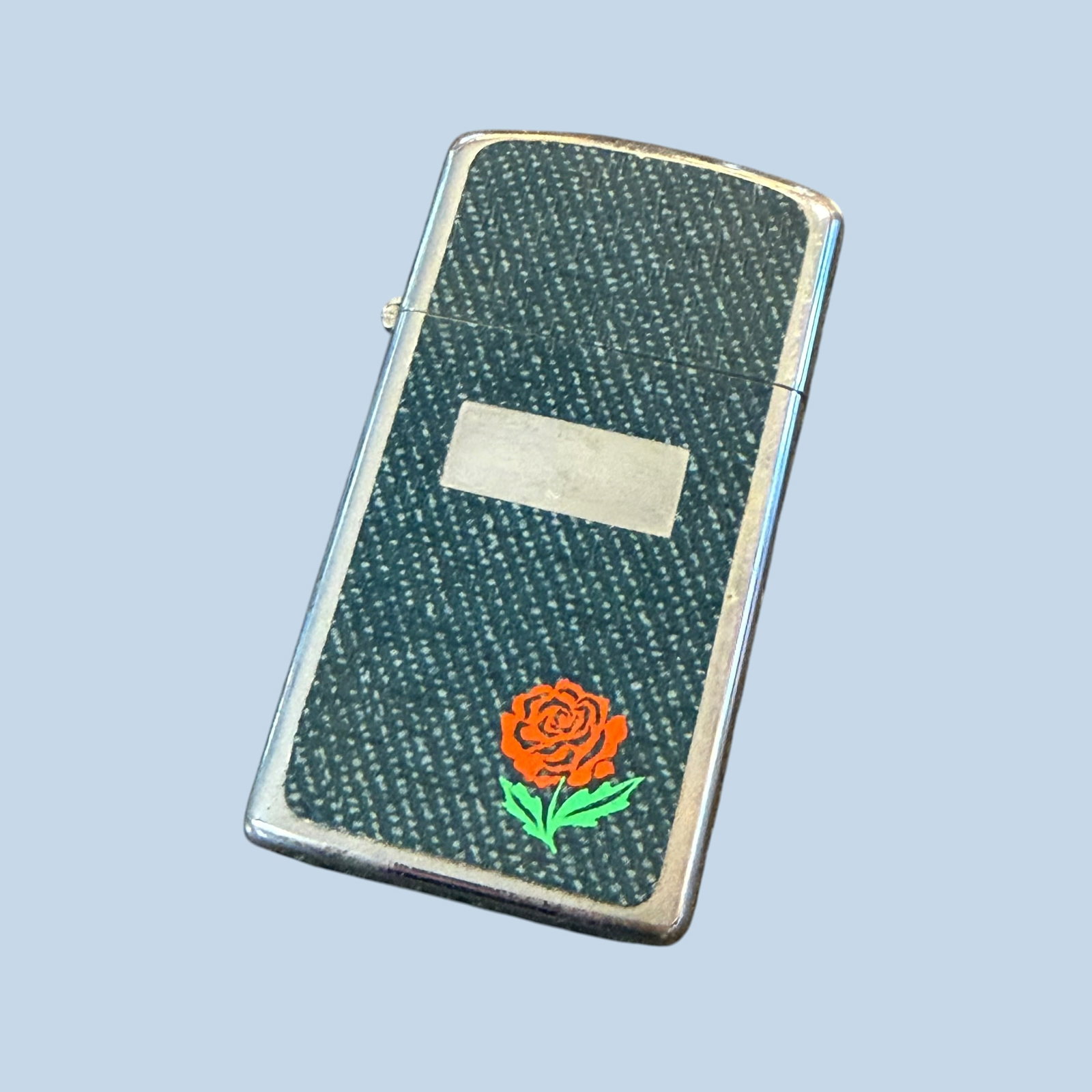 Vintage 1976 Zippo Slim Pocket Lighter Denim Rose Unfired Unused: Description: 1976 Zippo Slim lighter. Original denim with rose sticker/decal finish. Unused unfired. Minimal finish wear on hinge side. / Material: Metal. / Size: 2 3/16” x 1 1/8” x 3/8&rd