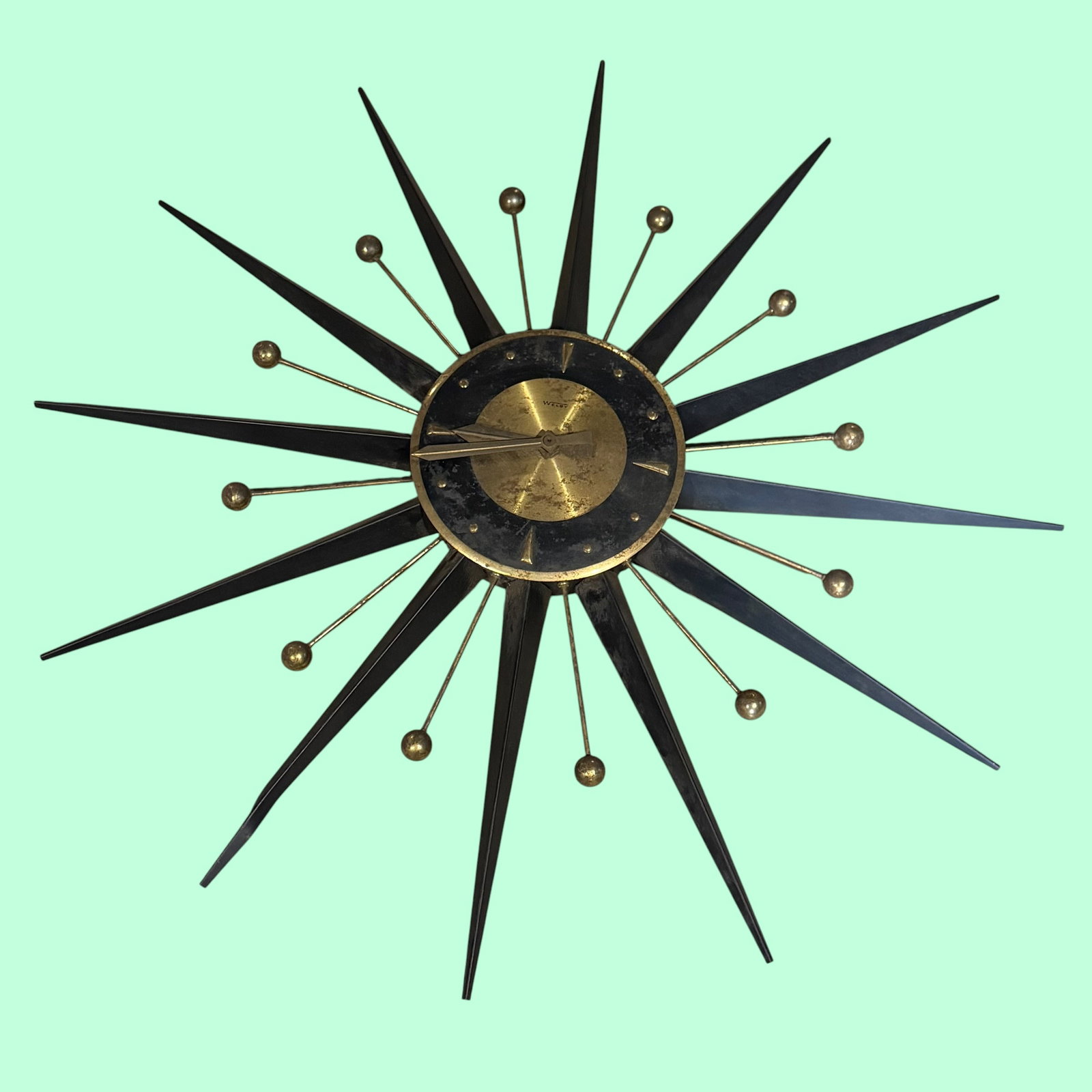 MCM Mid Century Modern Welby Sunburst Wall Clock 26”: Description: Mid Century Modern Welby made wall clock with Sunburst pattern. Black and cold tone in color. All metal. / One of the black points does have a bend at the end. Likely one should be able t