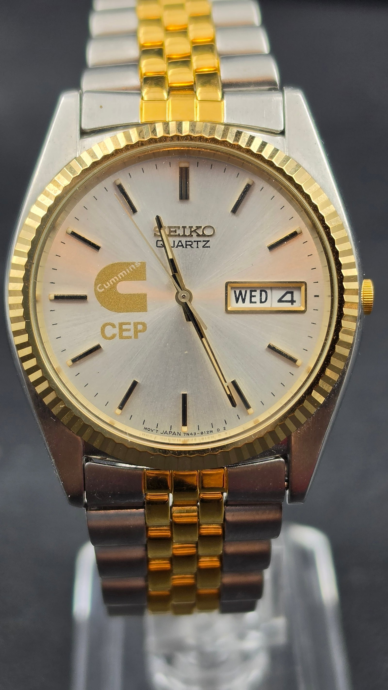Vintage 1990s Seiko Quartz Day-Date 7N43-8111 Two-Tone Cummins CEP Corporate Logo Dial Running NOS: This is a Seiko quartz day-date wristwatch, reference 7N43-8111, featuring a champagne sunburst dial with an applied gold-tone Cummins Engine Company logo and "CEP" designation printed on the dial fac