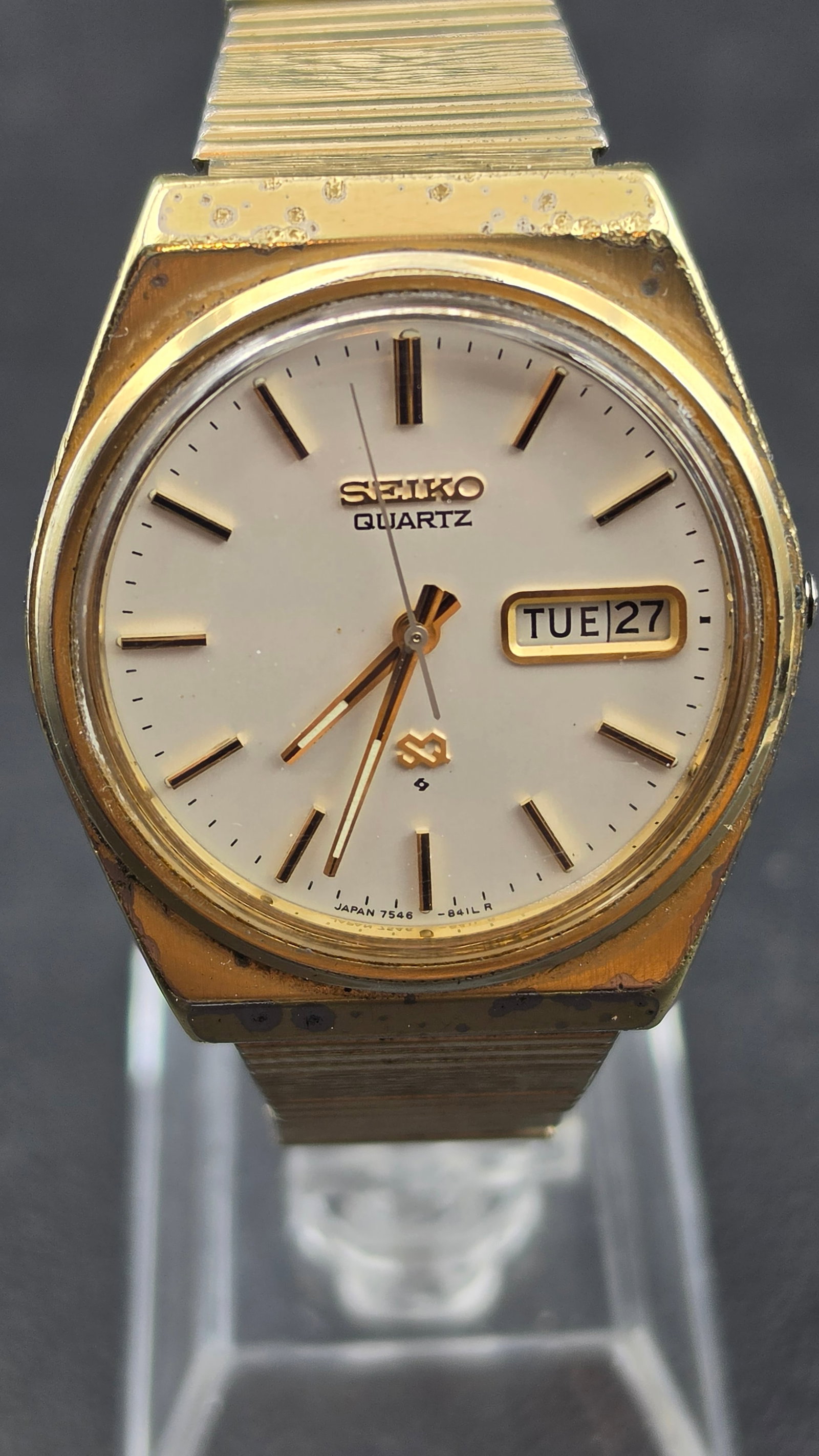 Vintage Seiko Quartz Day-Date Mens Wristwatch 7546-8419 1970s: This is a vintage Seiko Quartz men's wristwatch with a gold tone case. The dial is signed Seiko, marked Quartz, with the Seiko "S" emblem logo, applied baton hour markers, and marked Japan 7546-841LR 