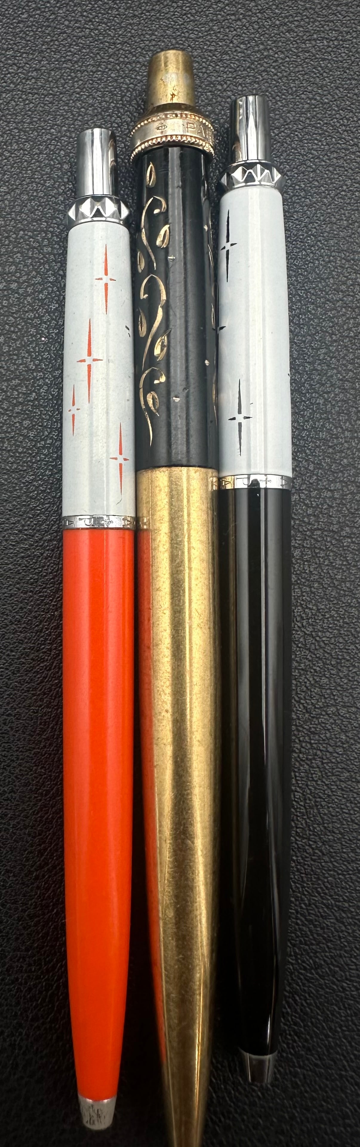 Vintage Parker Atomic Starburst Ballpoint Pens & Gold Tone Pen Lot of 3: Lot of three vintage pens including two Parker Atomic Starburst retractable ballpoint pens in red and black, plus one vintage gold-tone engraved retractable ballpoint pen. All show age-related wear an