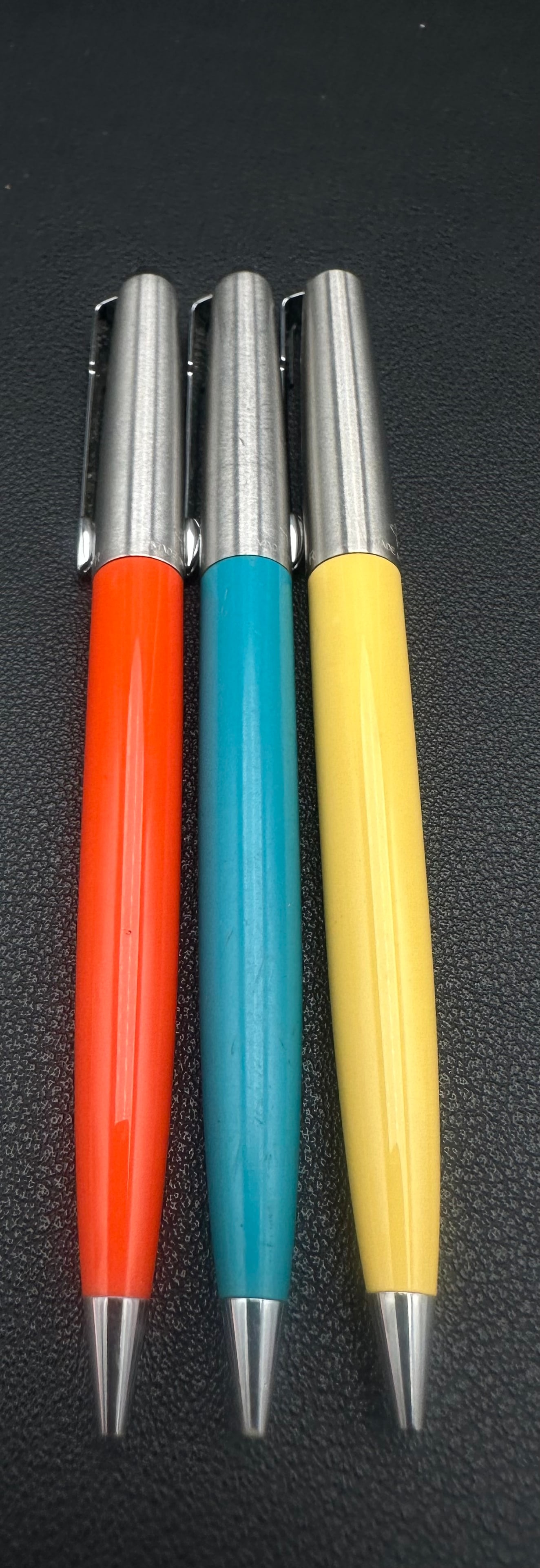 Vintage Parker Jotter Ballpoint Pen Lot of 3 Red Blue Yellow Stainless Caps: Lot of three vintage Parker Jotter ballpoint pens featuring colorful plastic barrels in red, blue, and yellow with brushed stainless steel caps and chrome trim. These classic retractable Jotters date 