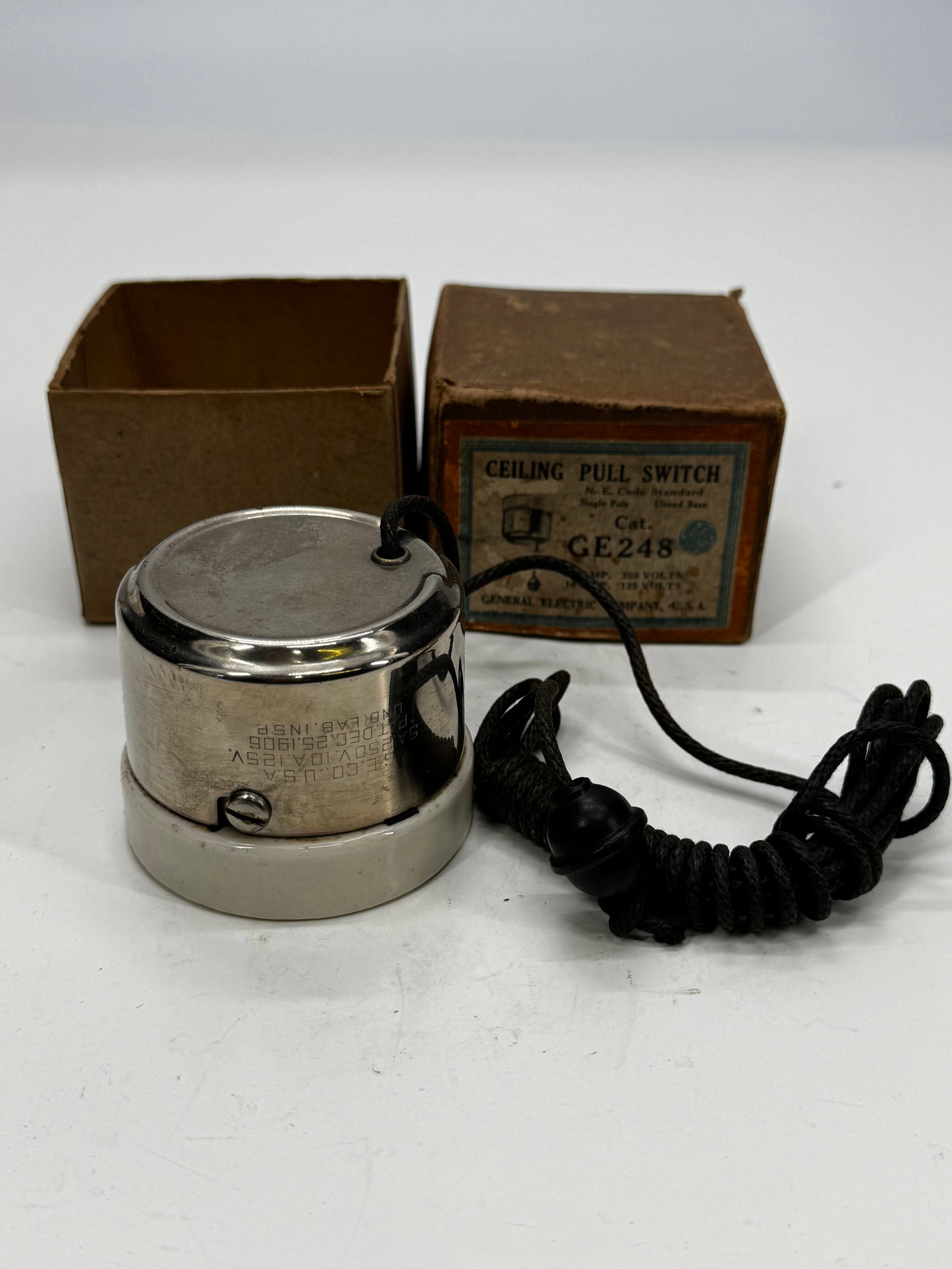 Vintage GE Porcelain Ceiling Pull Switch GE Co. USA w/ Original Box: Vintage General Electric ceiling pull switch featuring a white porcelain base, nickel-plated metal housing, and black braided pull cord with knob. Marked GE Co. U.S.A., rated 10A 125V / 5A 250V, with 
