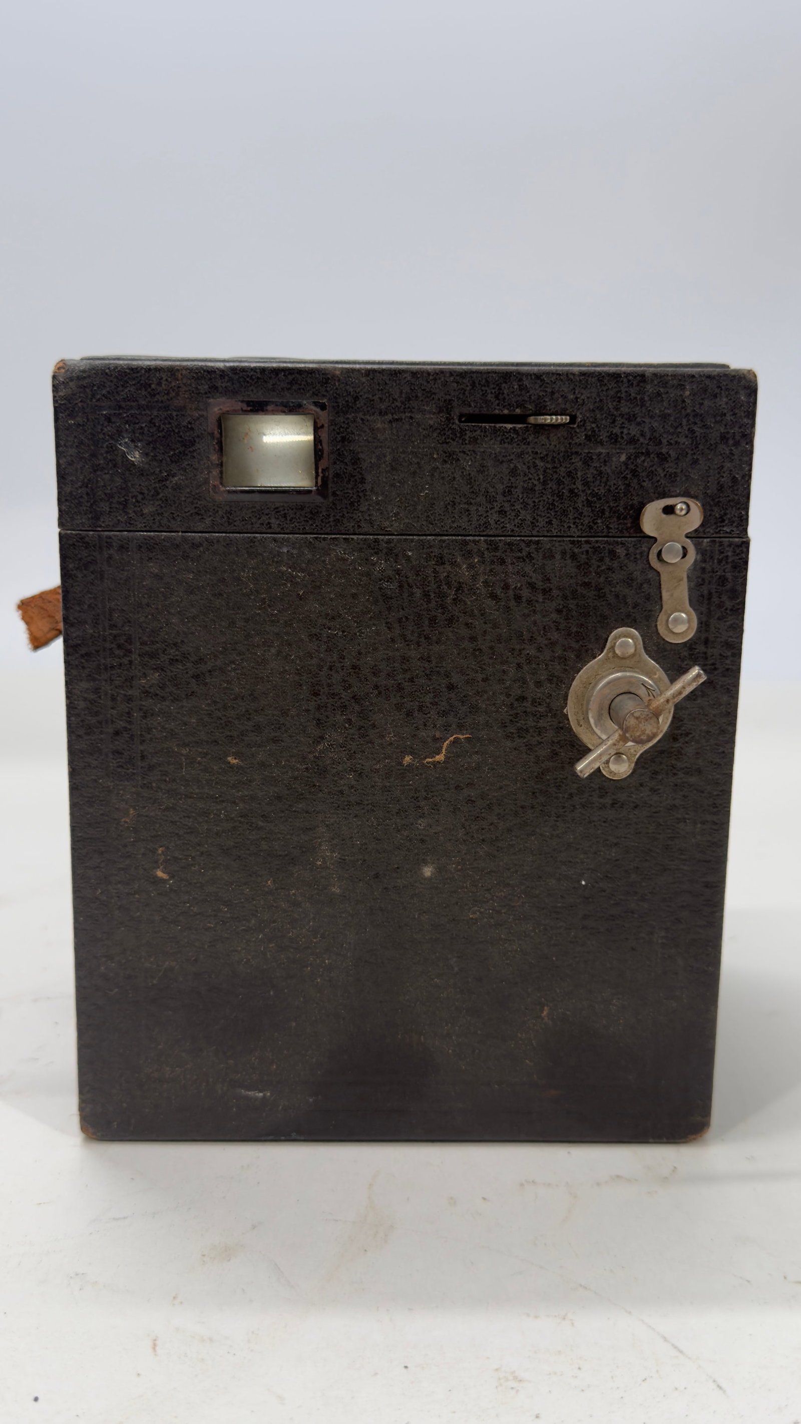 Antique Box Camera c. 1910–1920: Antique box camera with black leatherette-covered body, original viewfinders, winding key, and simple shutter controls. Features dual red film windows on the back for roll film advancement. An