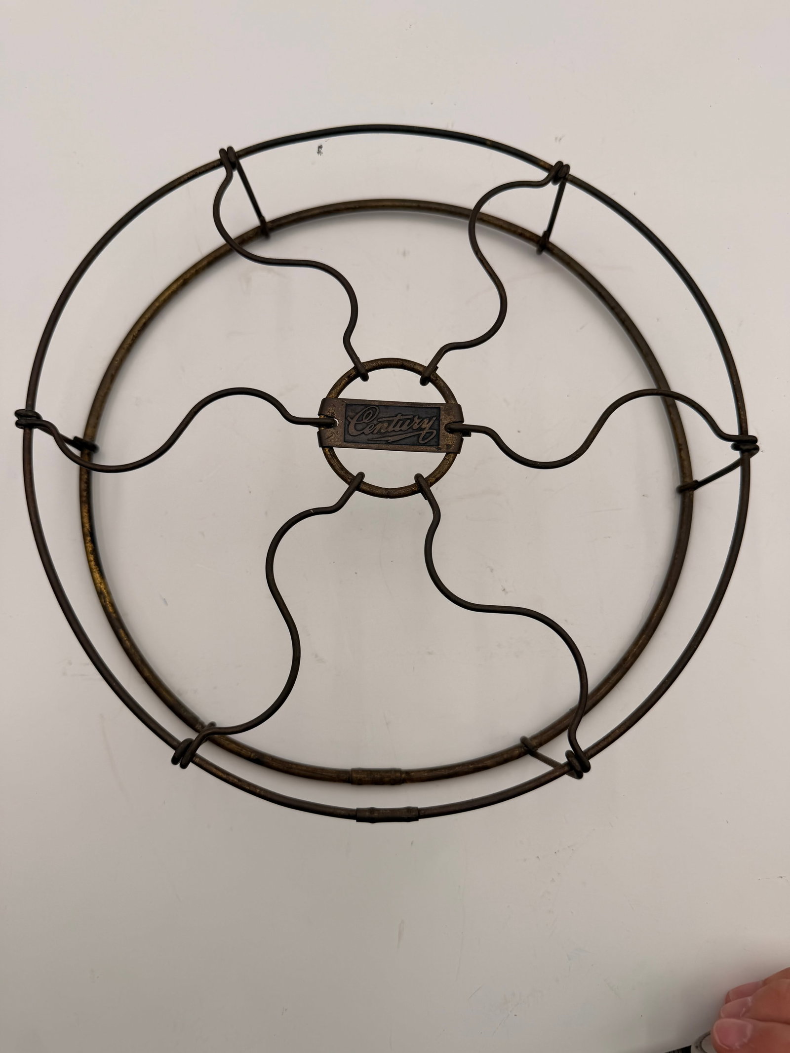 Vintage Century Electric Fan Front Guard: Original wire front guard from a Century Electric desk fan featuring the embossed Century center badge. Constructed of heavy steel wire with an aged bronze finish and distinctive wavy spoke design.