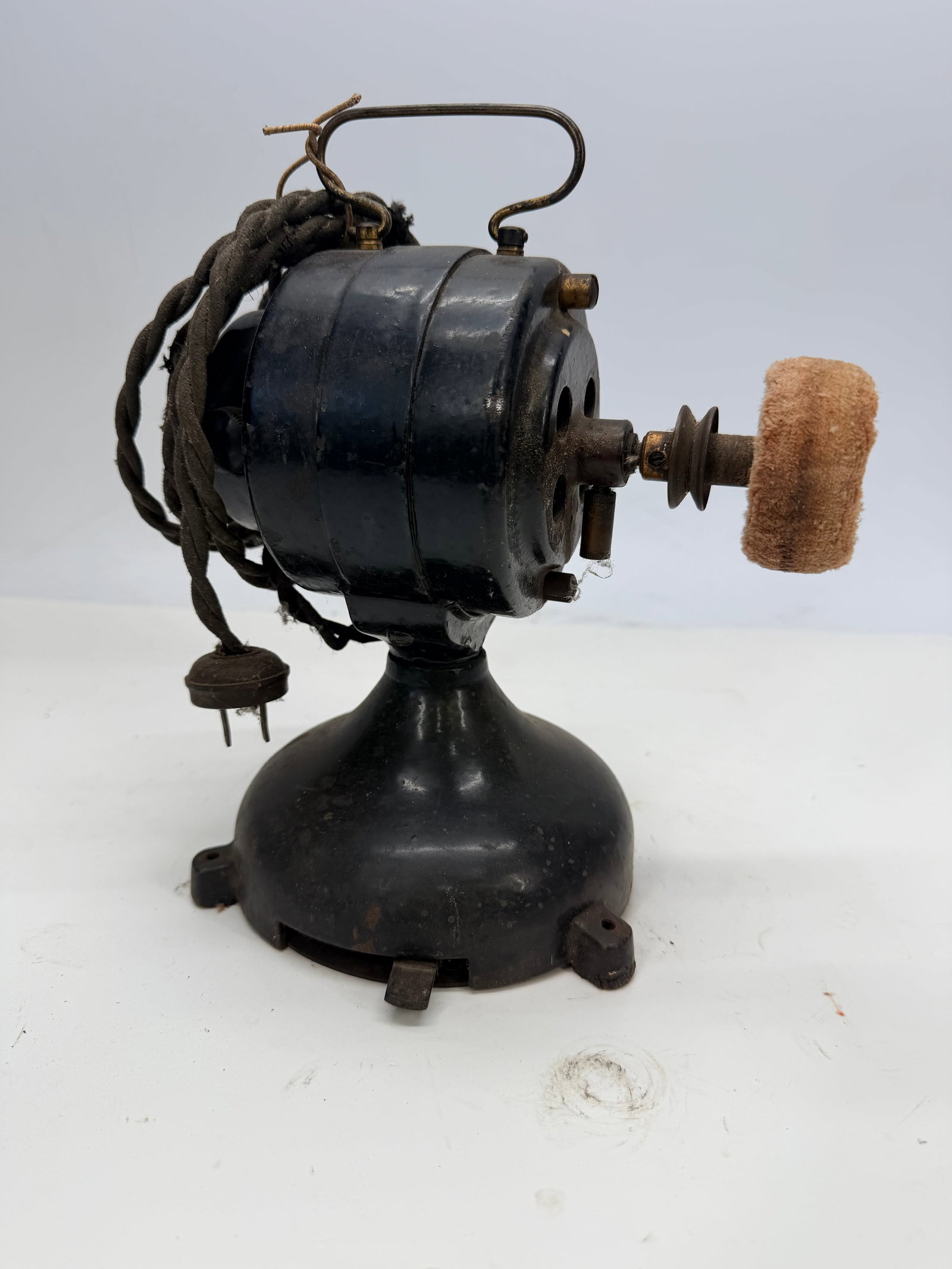 Antique black cast iron motor: This antique black cast iron motor resembles parts from early 20th-century electric fans.It has been modified with a small buffing wheel attached to the motor shaft, rather than its original fan blade