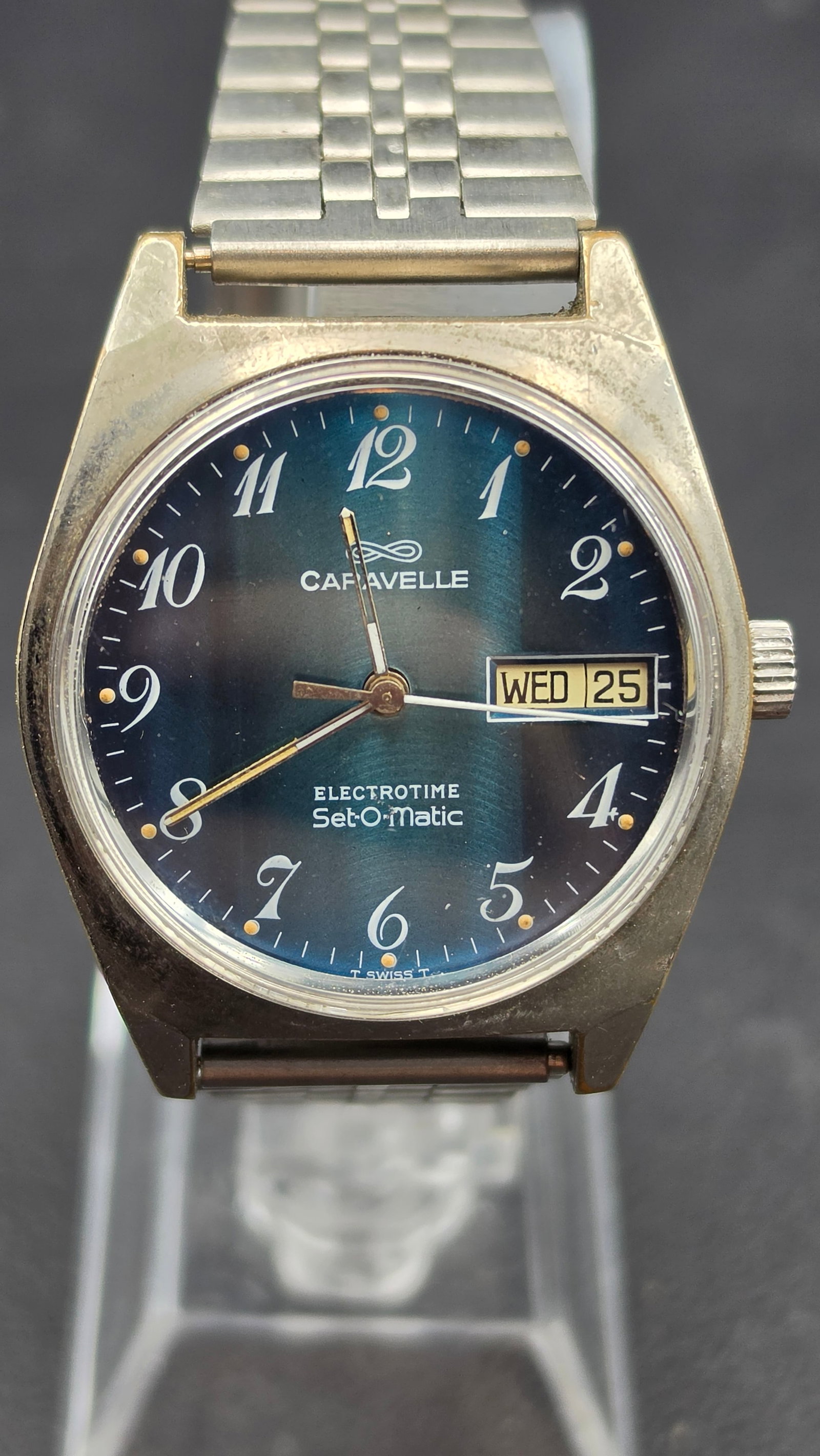 1970s Caravelle Electrotime Set-O-Matic Blue Dial Day-Date Wristwatch 35.55mm Hybrid Movement: This is a vintage Caravelle Electrotime Set-O-Matic wristwatch in a stainless steel case with base metal bezel, measuring 35.55mm in diameter. The blue sunburst dial is signed CARAVELLE with white Ara