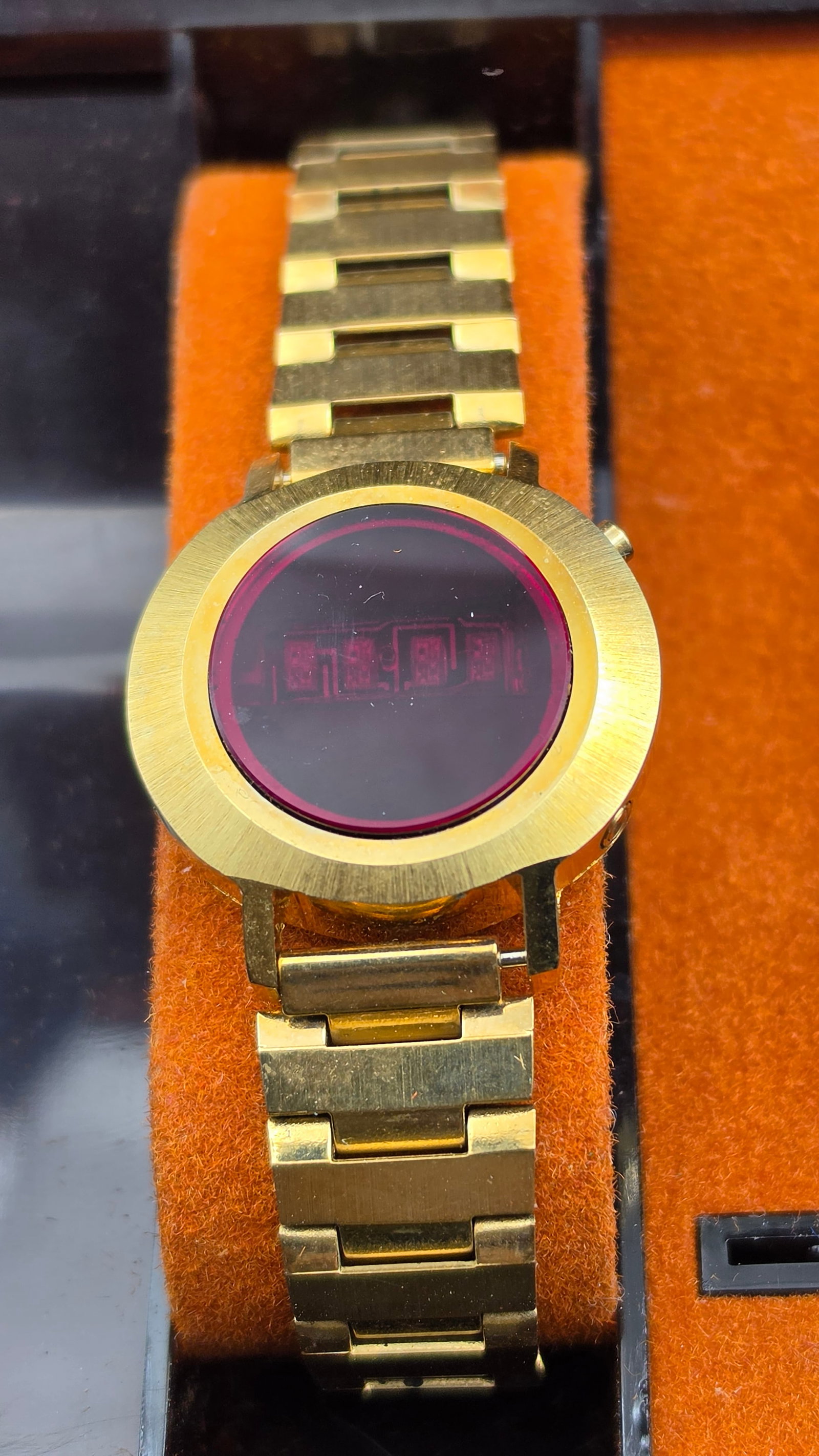 Vintage 1970s Unitrex Red LED Digital Watch Gold Tone with Original Smoked Lucite Box: This is a vintage 1970s Unitrex red LED digital wristwatch with a round gold-tone case. The watch face features a smoked red display window that reveals the red LED digital segments when active. The c
