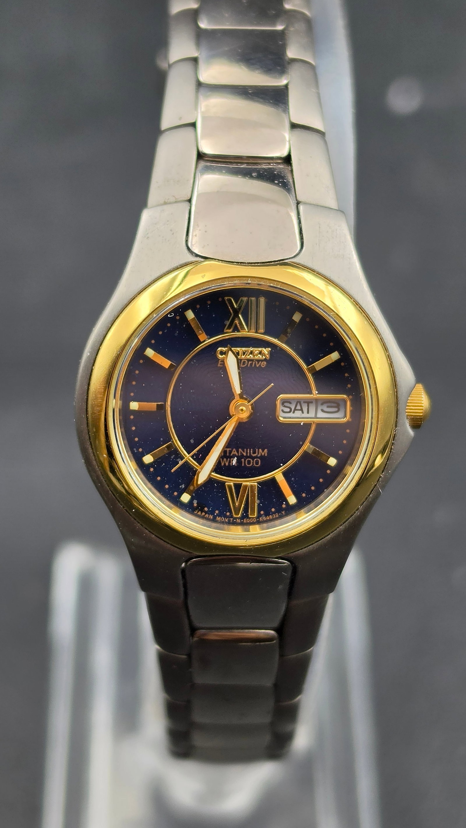 Citizen Eco-Drive Titanium WR100 Ladies Watch, Blue Dial, Day Date, Two Tone Bezel: Vintage Citizen Eco-Drive wristwatch in a titanium case measuring approximately 25.5mm, with a gold tone bezel and stainless steel bracelet. Blue textured dial signed Citizen, Eco-Drive, Titanium, WR 