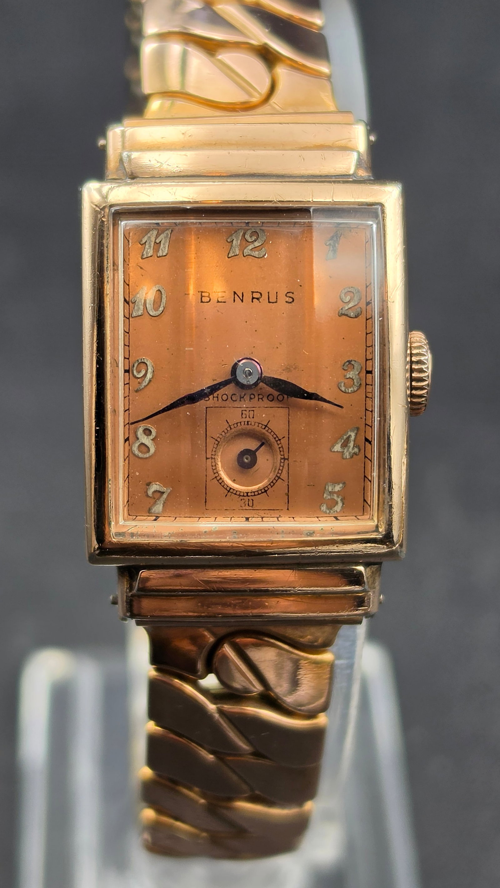 1940s Benrus Art Deco Rectangular Watch 17 Jewels Model AK16 Rose Gold Filled Salmon Dial: This is a vintage Benrus Art Deco rectangular wristwatch from the 1940s in a rose gold filled case, measuring approximately 21mm across. The salmon toned dial reads Benrus, Shockproof, with applied si